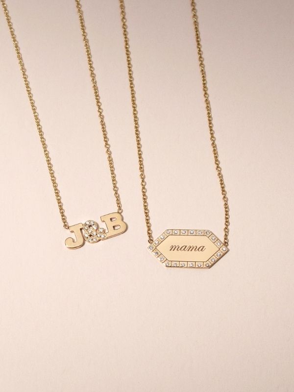 Two personalized necklaces are laying down on a blush background