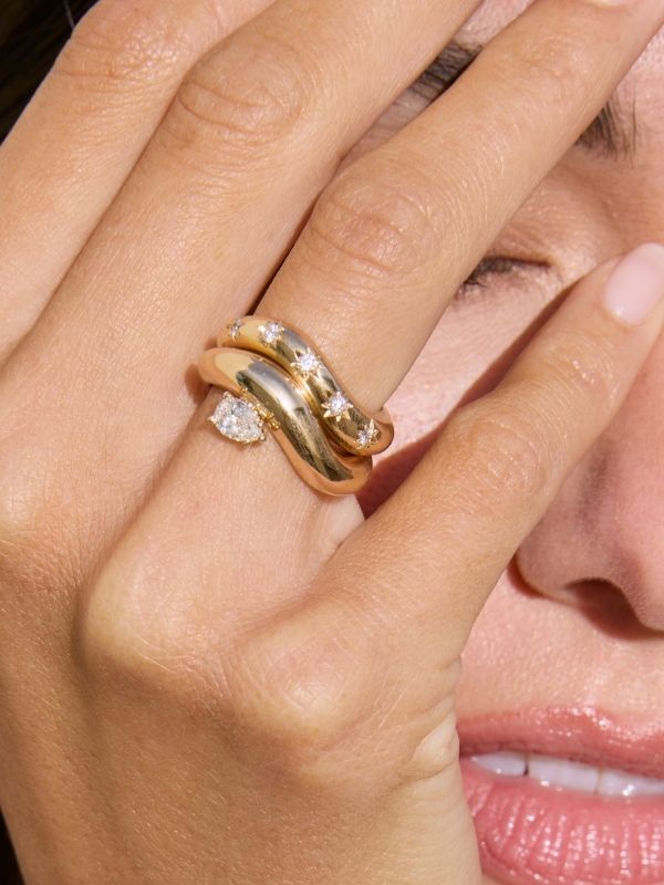 A woman covers her face with her hand to reveal two wave rings that make a perfect luxury gift.