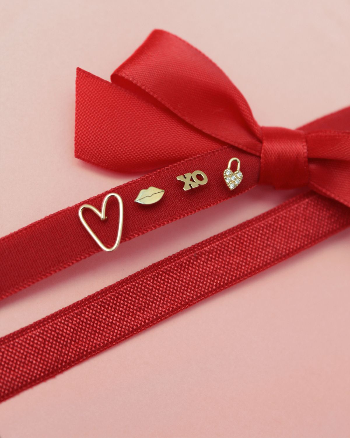 four different Zoe Chicco 14k gold stud earrings laying on a red velvet ribbon against a pink background