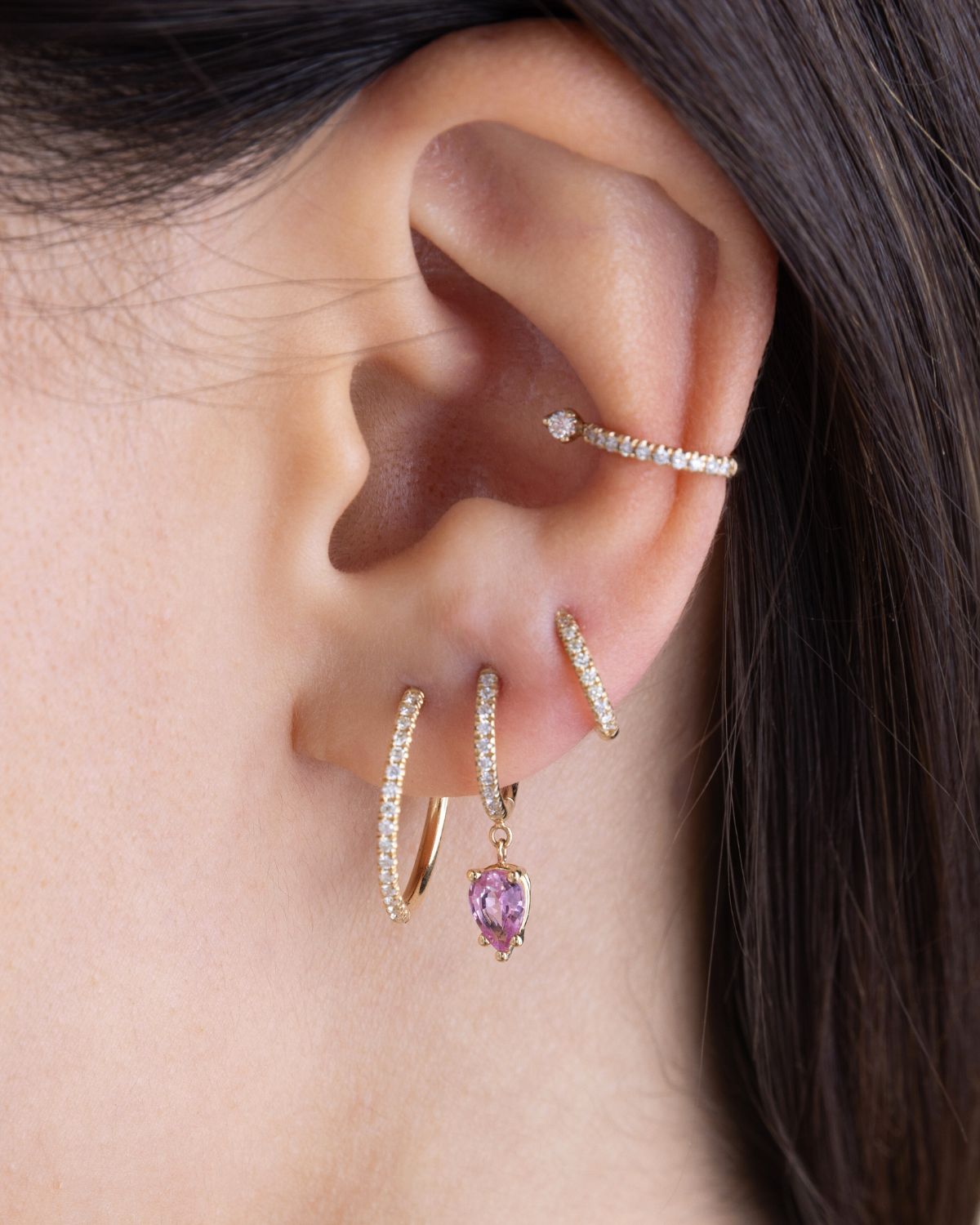 woman's ear wearing multiple 14k gold and pavé diamond earrings