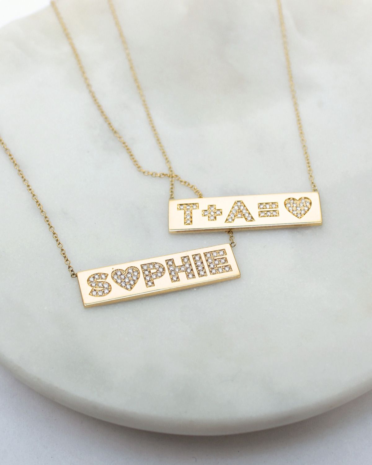 Two Zoë Chicco 14k gold and diamond personalized ID necklaces laying on a marble tray