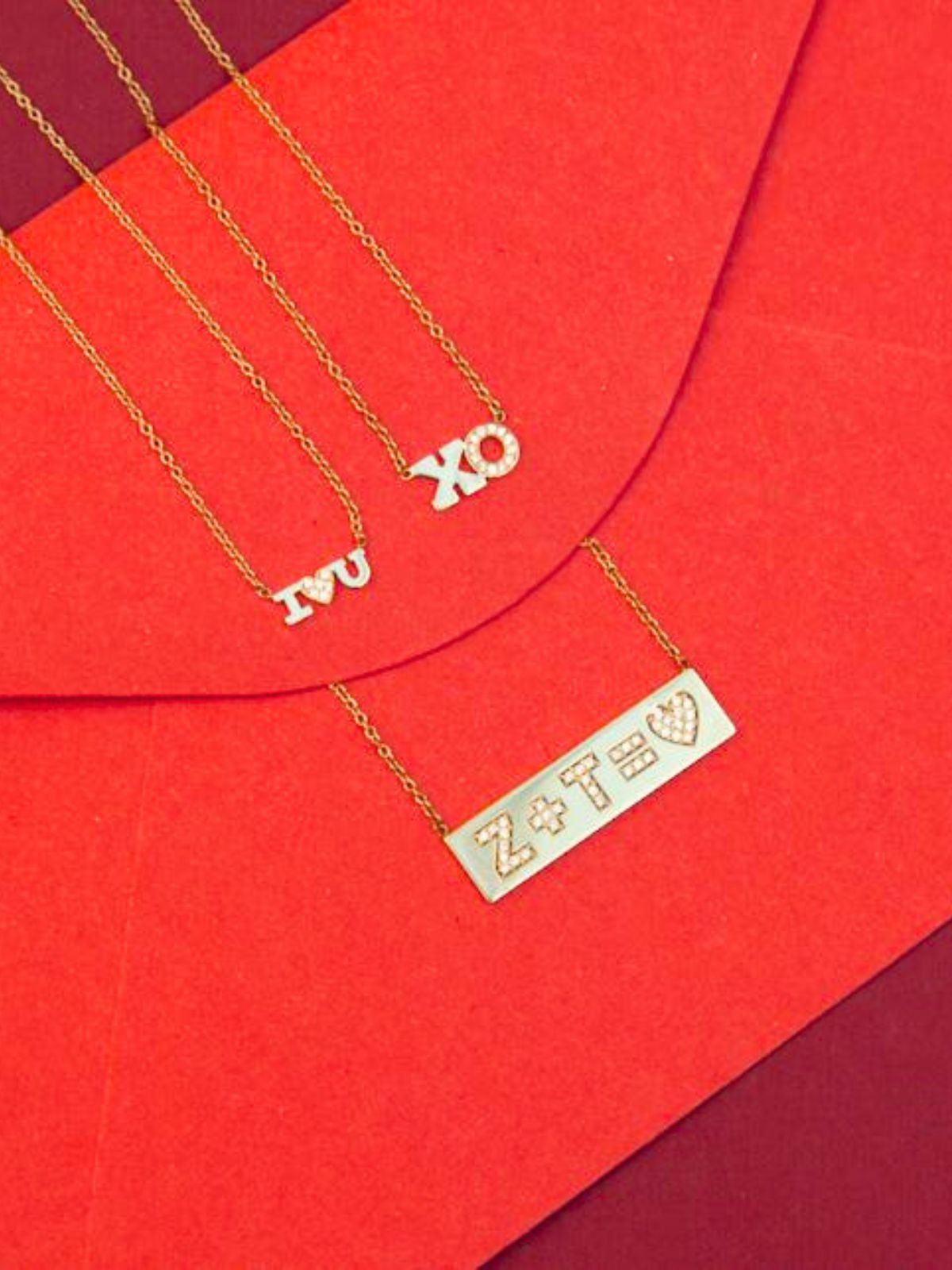 Two Zoë Chicco 14k gold and diamond personalized ID necklaces laying on a marble tray
