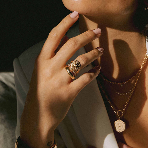 woman in white blazer resting her hand on her chin wearing a Zoë Chicco 14k Gold Lion Head with Diamond Eyes Wide Band Ring and Half Round Band on her ring finger