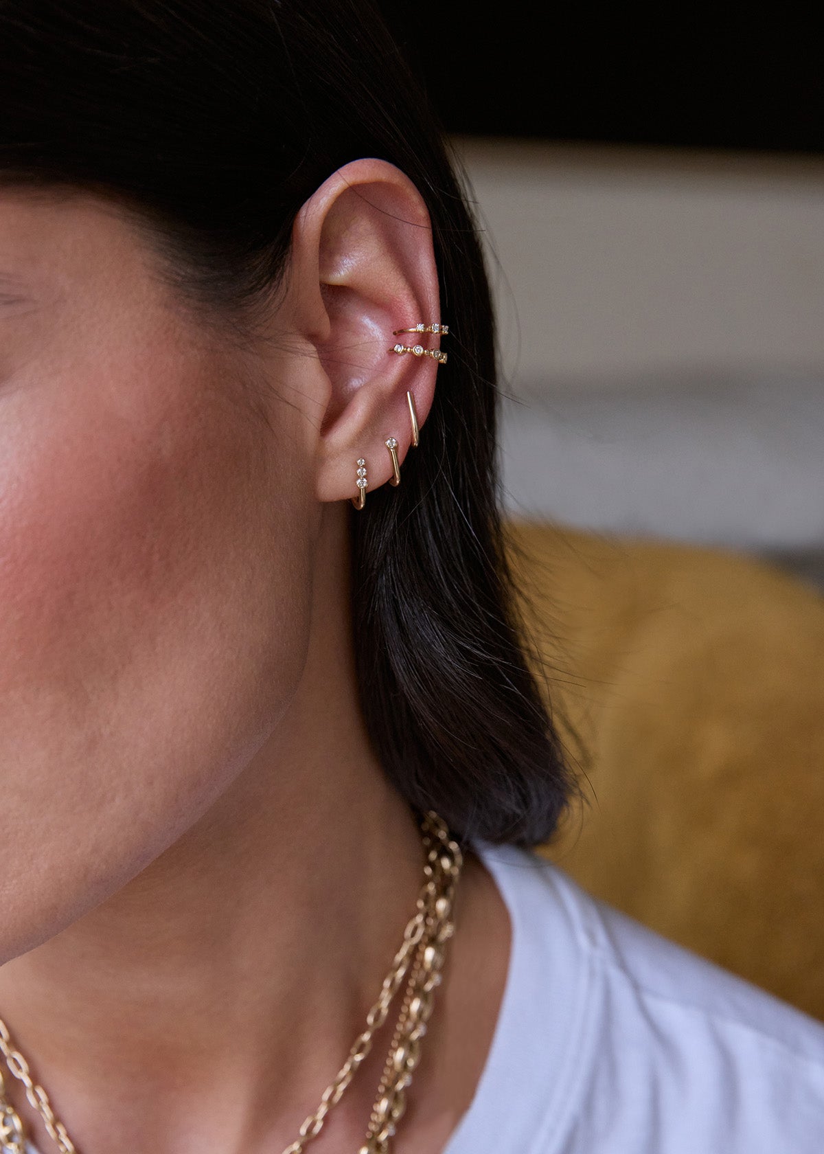 Close-up of an ear wearing Zoe Chicco 14k gold and diamond J hook earrings and bezel ear cuffs with a blurred background