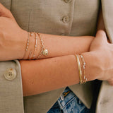 woman in an olive vest with her hands crossed in front of her wearing a Zoë Chicco 14k Gold Pavé Diamond Line Knife Edge Cuff Bracelet stacked with two other diamond bracelets on her wrist