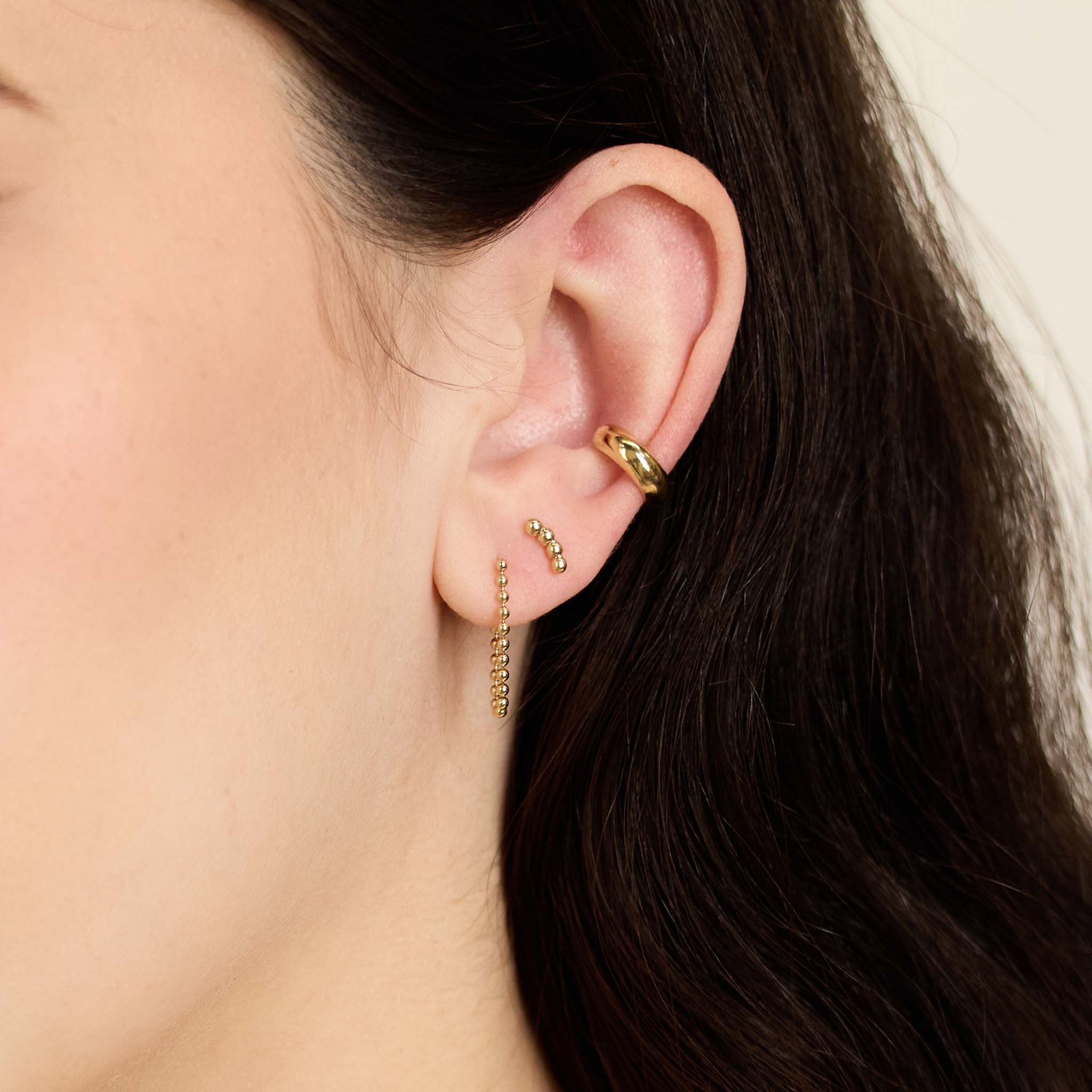 close up of a woman's ear wearing a Zoë Chicco 14k Gold Small Beaded Curve Stud Earring in her second piercing layered with a 14k Bead Chain Huggie Earring and Chubby Ear Cuff