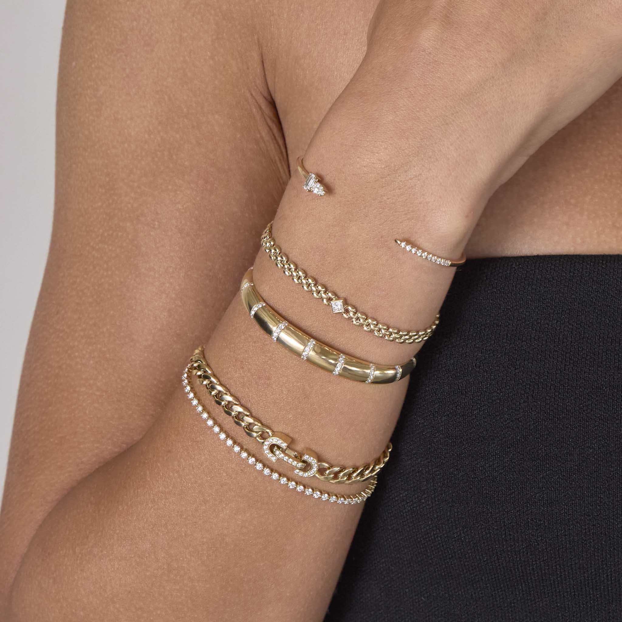 A woman is wearing a Zoe Chicco bracelet stack with the 14k Princess Diamond Small Panther Chain Bracelet, 14k Mixed Cut & Pavé Diamond Cuff, 14k Pavé Diamond Banded Small Aura Cuff, 14k Vintage Pavé Diamond Horsebit Link Large Curb Chain Bracelet and tennis bracelet