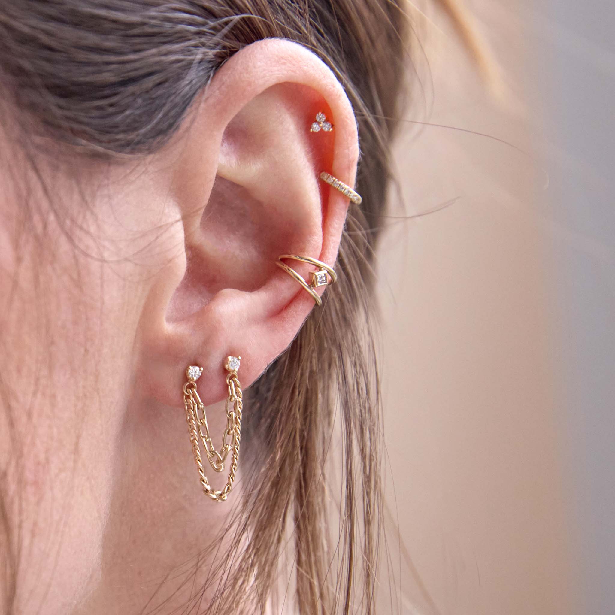 close up of a woman's ear wearing a Zoë Chicco 14k Gold Nested Princess Diamond Double Wire Ear Cuff layered with a 14k Prong Diamond & Mixed Chain Double Stud Earring and a pavé diamond hinge huggie hoop and Zoë Chicco 14k Gold Tiny Prong Diamond Trio Stud Earring