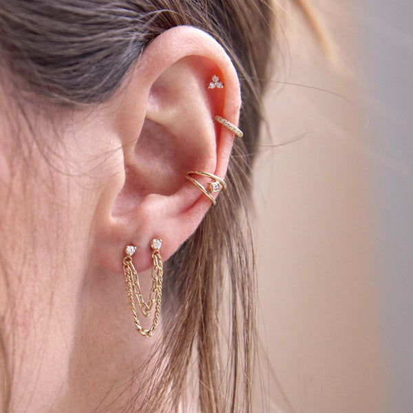 close up of a woman's ear wearing a Zoë Chicco 14k Gold Nested Princess Diamond Double Wire Ear Cuff  layered with a 14k Prong Diamond & Mixed Chain Double Stud Earring and a pavé diamond hinge huggie hoop and Zoë Chicco 14k Gold Tiny Prong Diamond Trio Stud Earring