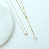 a Zoë Chicco 14k Gold Small Oval Link Chain Lariat with Pearl Drop laying flat against a white stone background