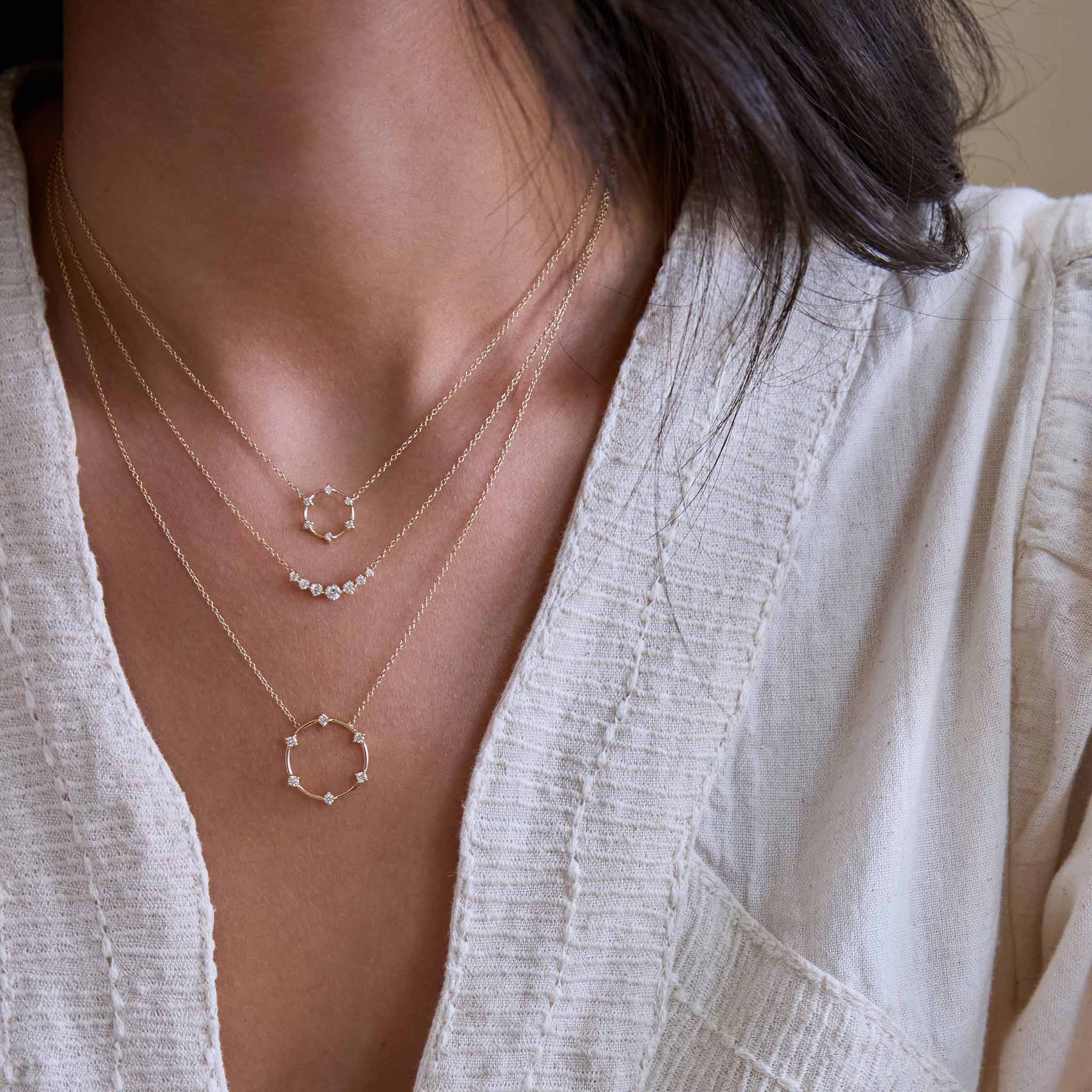 Zoe Chicco 14k gold open circle prong diamond necklaces worn around a woman's neck wearing a linen shirt