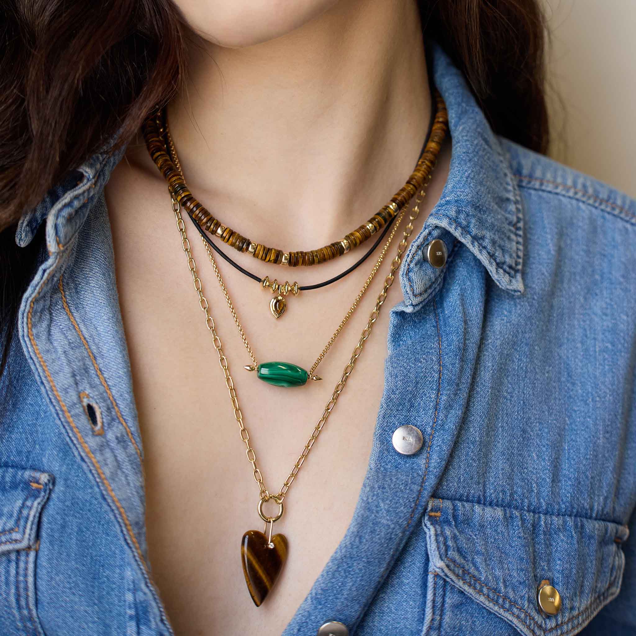 Person wearing layered necklaces with a denim jacket featuring 14k Tiger Eye Heart Pendant Medium Square Oval Chain Enhancer Necklace