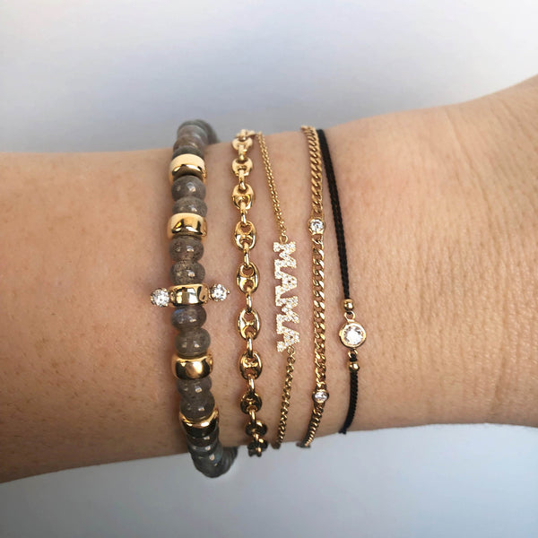 woman's wrist wearing a Zoë Chicco 14k Gold Floating Diamond Solitaire Black Cord Bracelet stacked with a labradorite bead bracelet and three gold bracelets