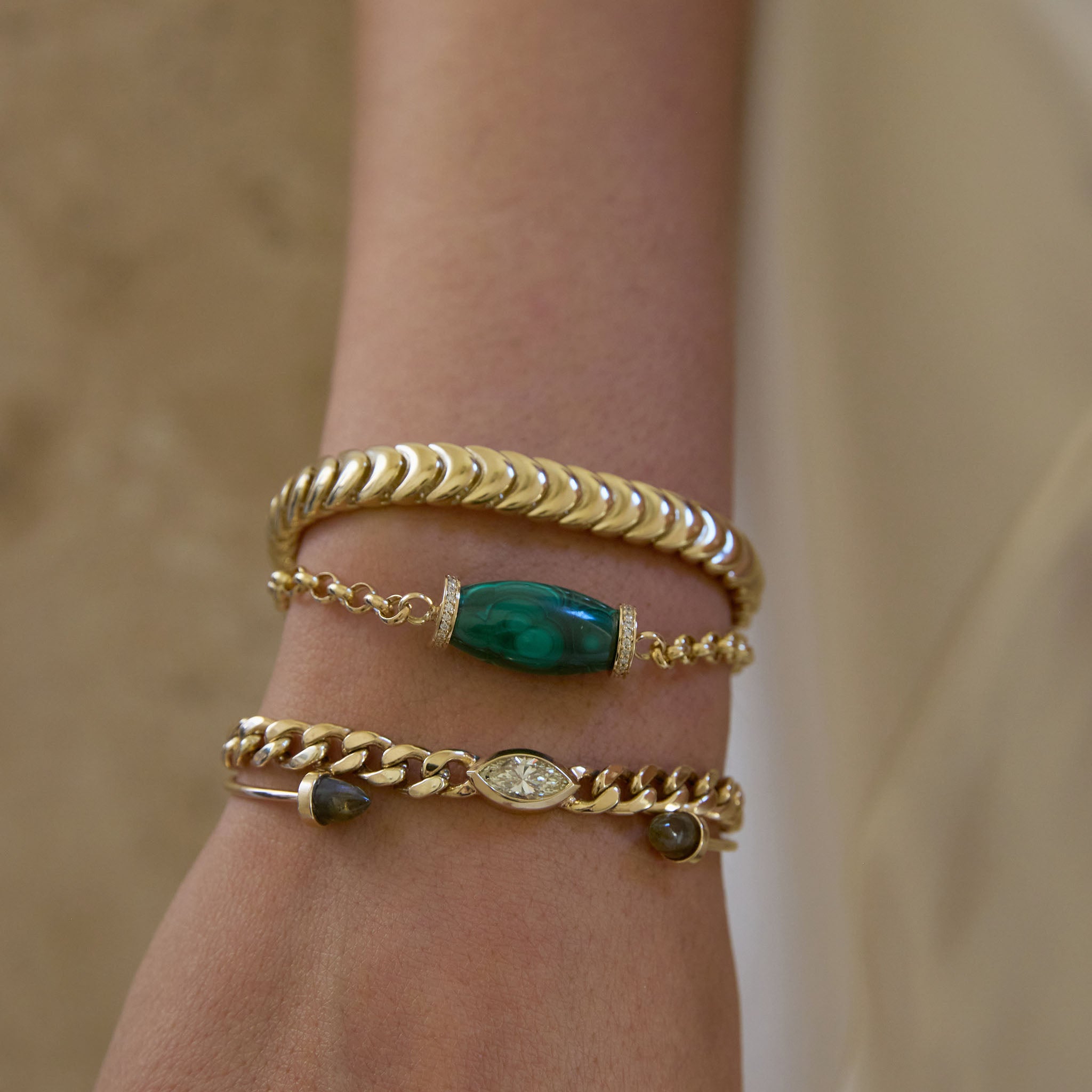 Close-up of a wrist wearing three Zoe Chicco 14k gold bracelets with green gemstones and a marquise diamonds
