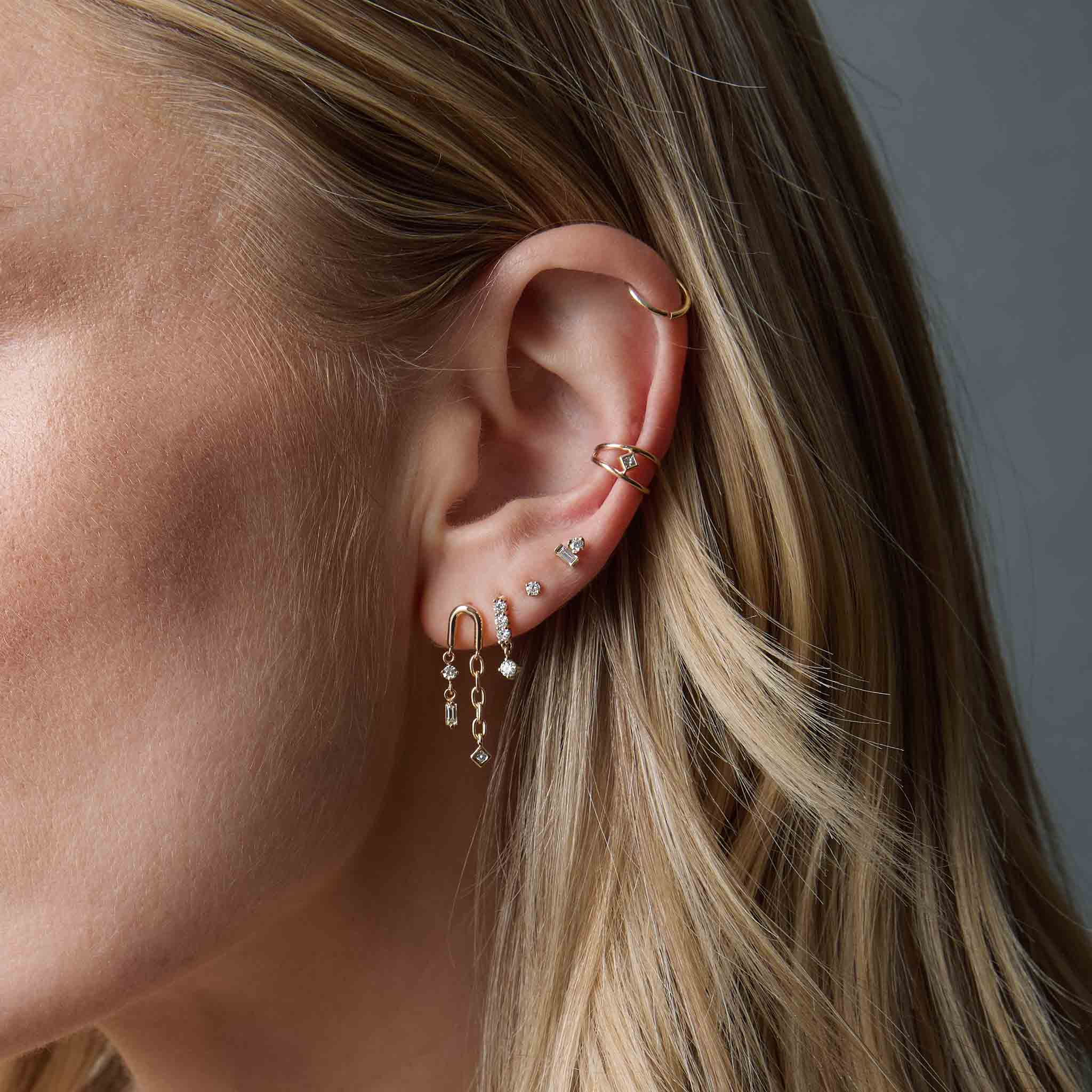 woman wearing a Zoë Chicco 14k Gold Nested Princess Diamond Double Wire Ear Cuff layered with a 14k Baguette & Prong Diamond Stacked Stud in her fourth piercing, and three other diamond earrings