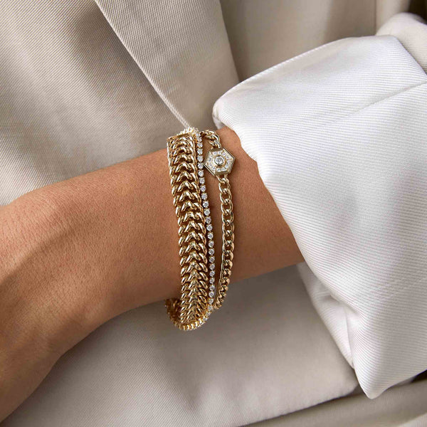 woman in a beige blazer wearing a Zoë Chicco 14k Gold Medium Curb Chain Diamond Hexagon Halo Bracelet on her wrist layered with two other bracelets
