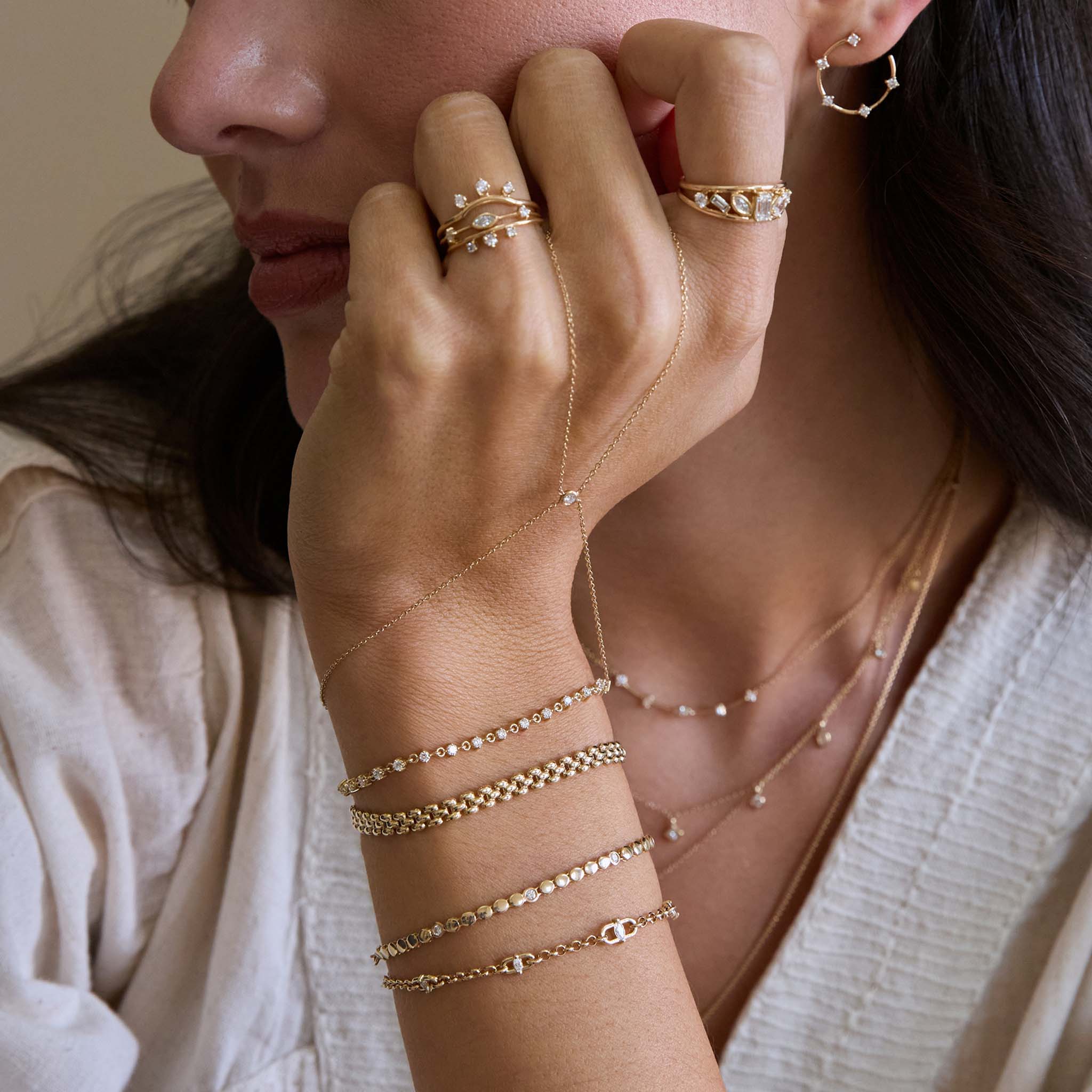 Close-up of a person wearing Zoe Chicco 14k gold and diamond jewelry including rings, bracelets, earrings, and hand chain.