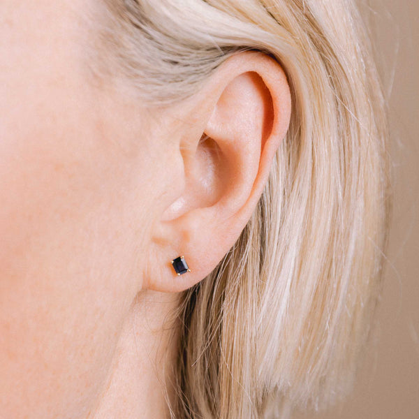 close up image of a woman's ear wearing a Zoë Chicco 14k Gold Emerald Cut Blue Sapphire Stud Earring