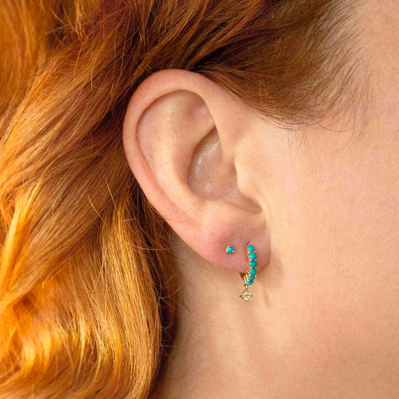 close up of a woman's ear wearing a Zoë Chicco 14k Gold Dangling Diamond Prong Set Turquoise Hinge Huggie Hoop Earring layered with a small single turquoise stud in her second piercing