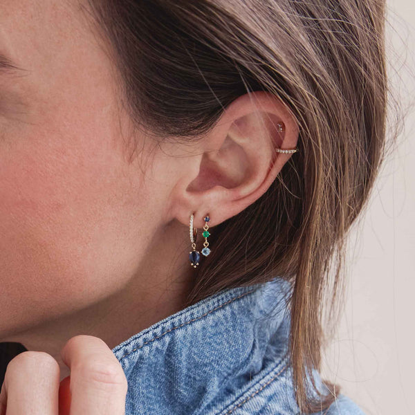 woman in a denim jacket wearing a Zoë Chicco 14k Gold Small Pavé Diamond Hinge Huggie Hoop with Pear Blue Sapphire and a 14k Linked Graduated Blue Ombre Gemstone Drop Earring stacked together on her ear