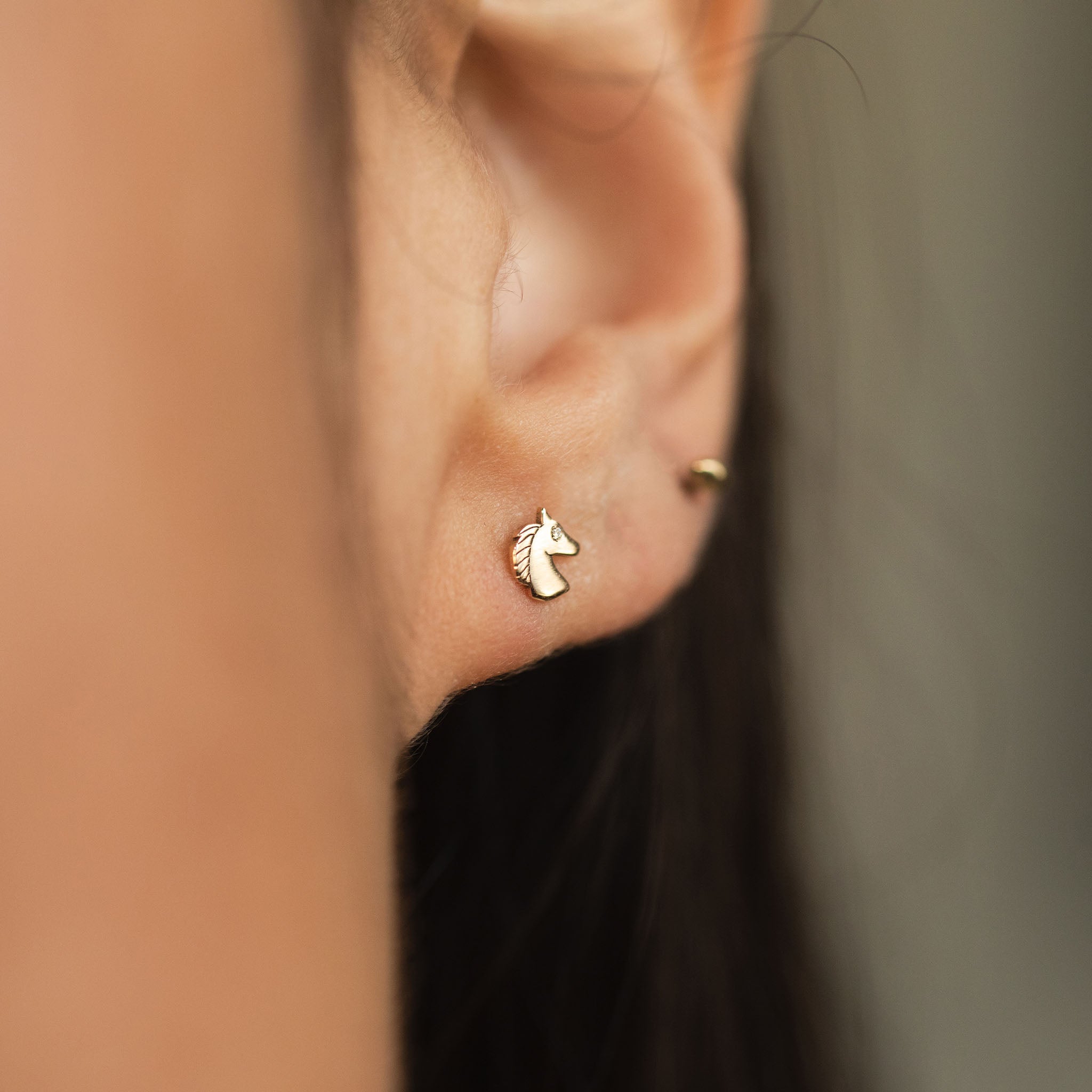 Gold horse-shaped earring with diamond eye is on a person's ear with a blurred background