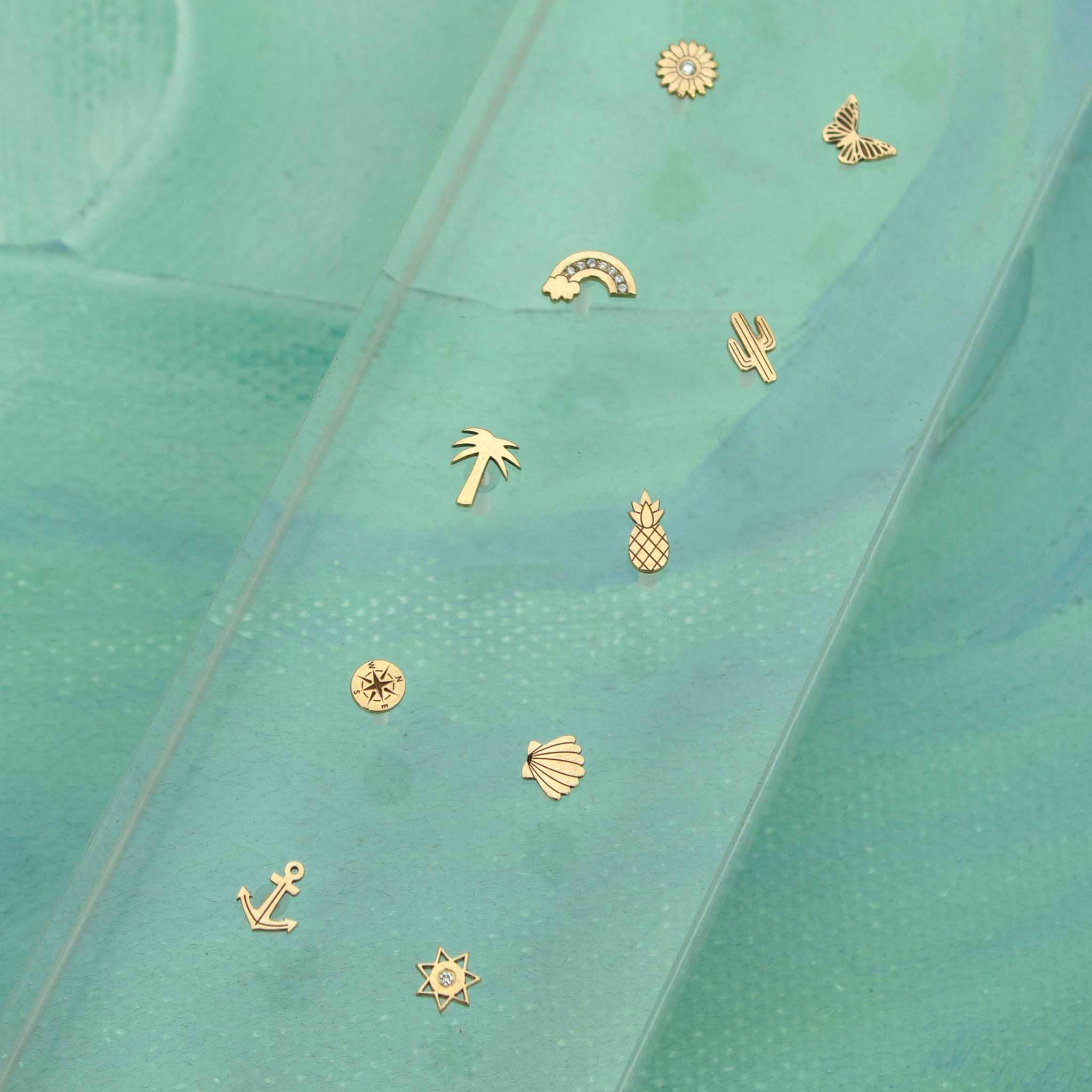 Gold Itty Bitty Symbol Studs on a turquoise background