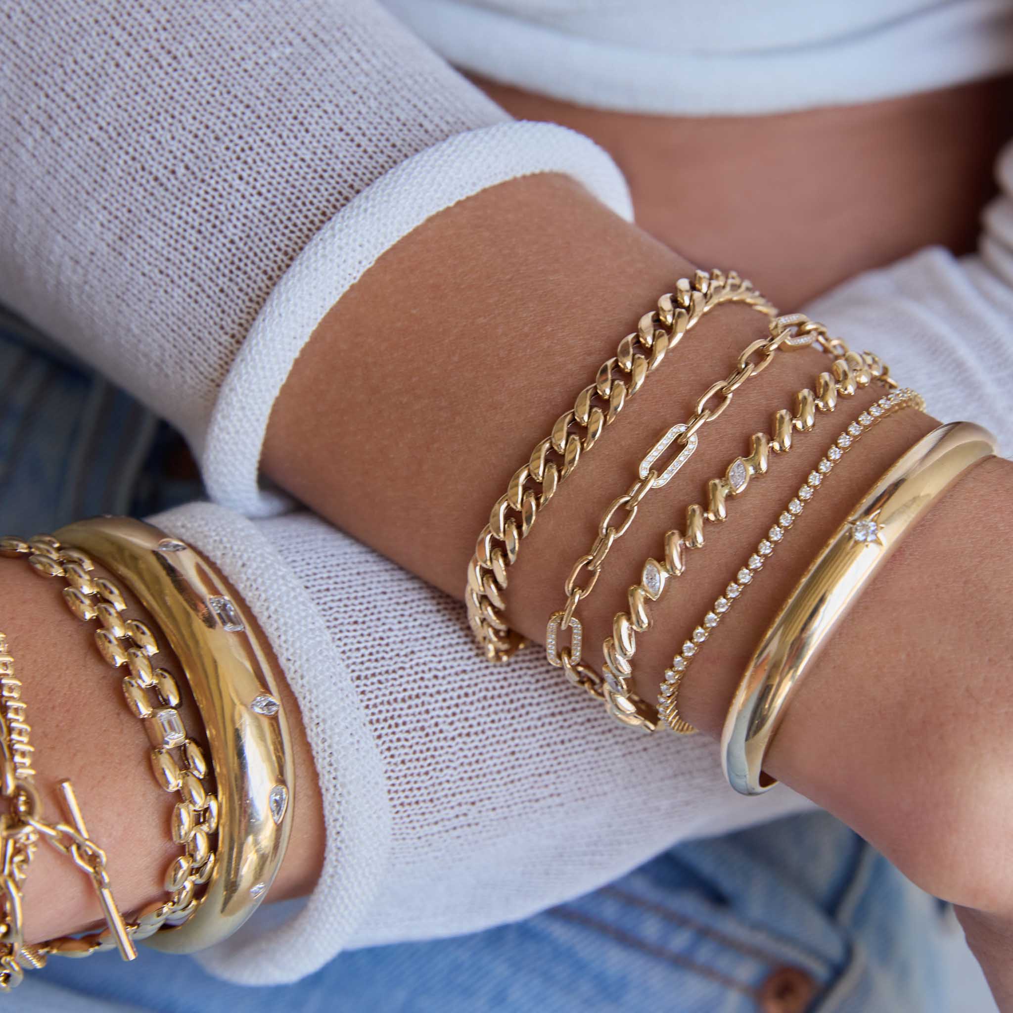 woman with her arms crossed wearing a Zoë Chicco 14k Gold 5 Marquise Diamond Station San Marco Chain Bracelet stacked with a Diamond Tennis Bracelet, Star Set Diamond Aura Cuff, 14k Medium Square Oval Chain Bracelet with 5 Pavé Diamond Links, and a Large Curb Chain Bracelet