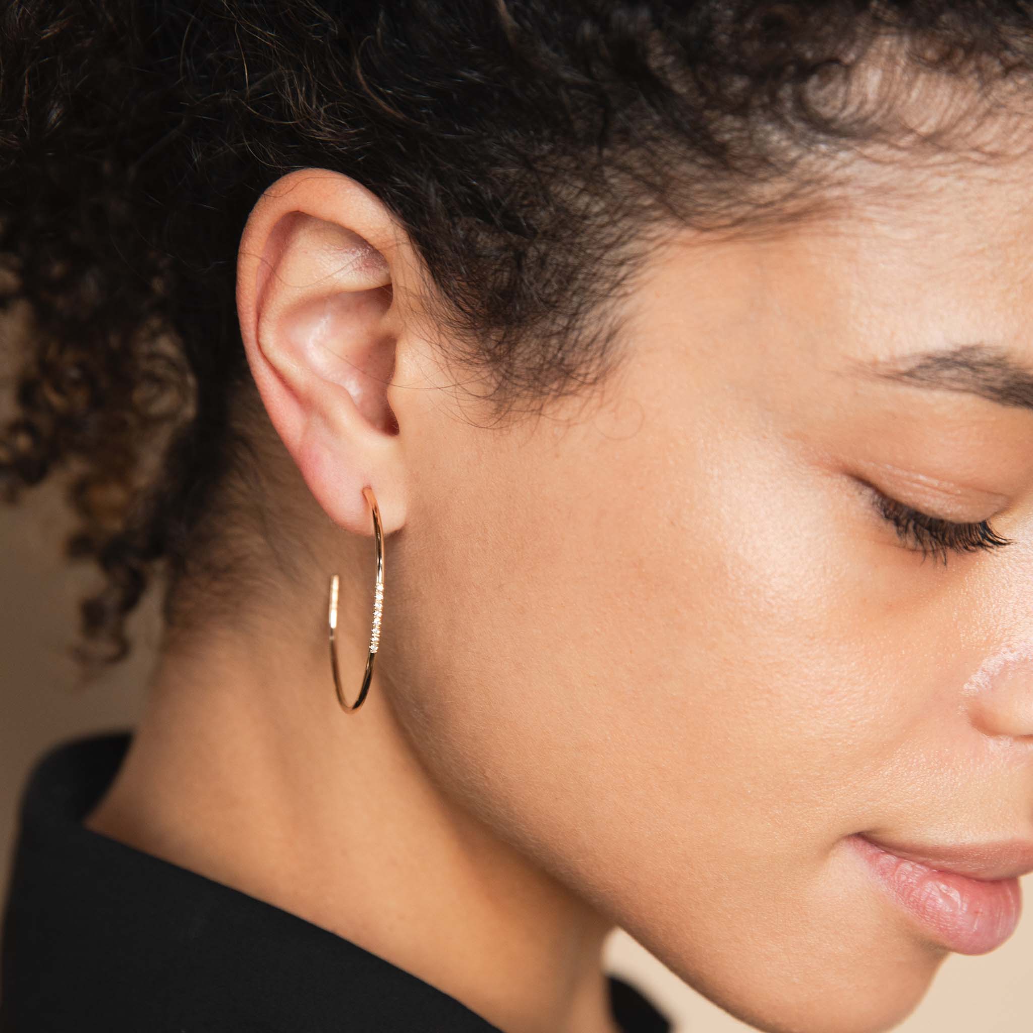 A woman wears a pair of Zoe Chicco Large hoops with 8 pave diamonds on the front.