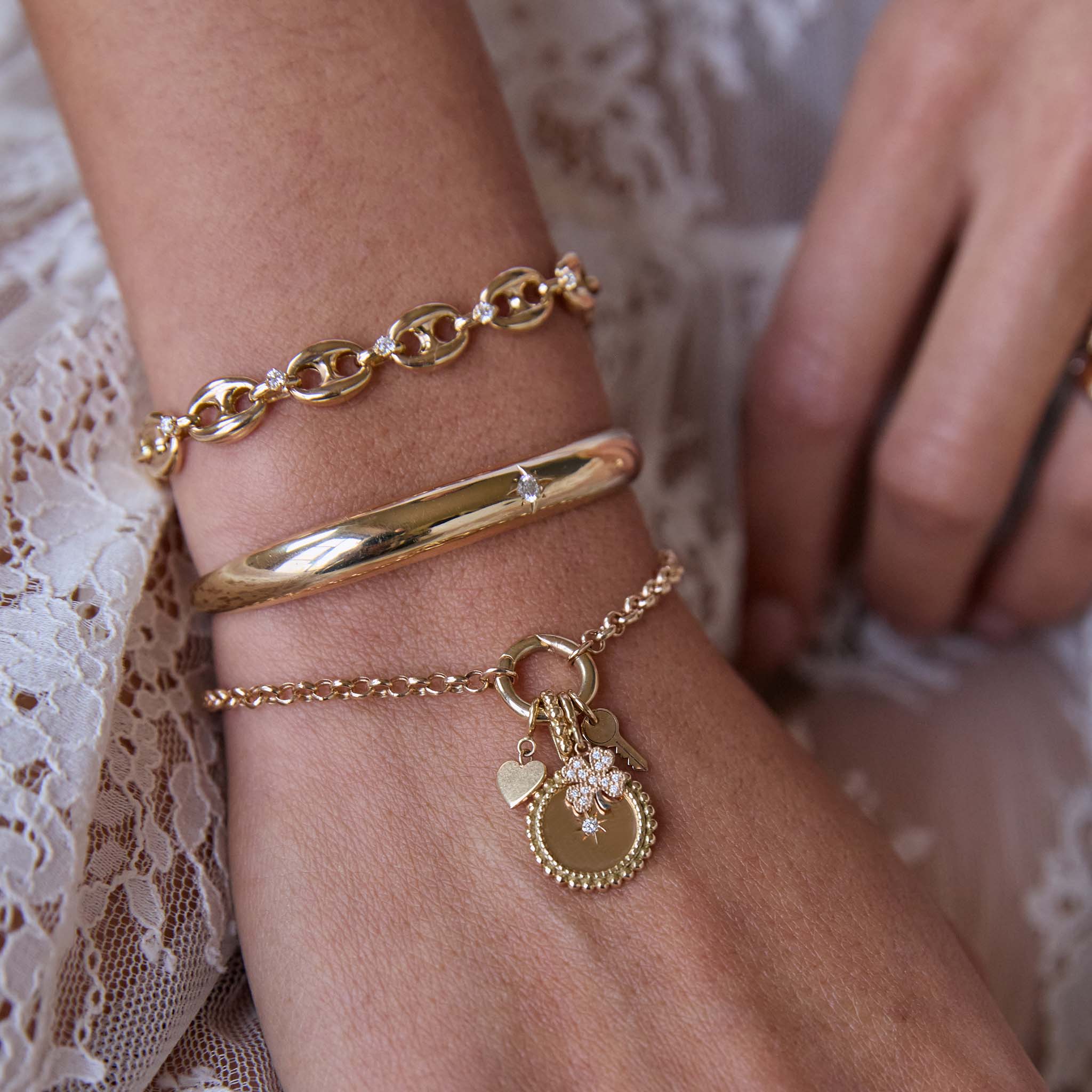 Zoe Chicco 14k Gold bracelets with charms and diamonds on a wrist against a lace background