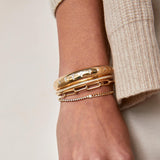 woman's wrist against a beige background wearing a Zoë Chicco 14k Gold Floating Diamond Mixed Curb Chain & Diamond Tennis Bracelet layered with two cuffs and a large paperclip link chain bracelet