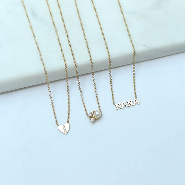 a Zoë Chicco 14k Gold Itty Bitty NANA Necklace laying against a marble tray with two other necklaces