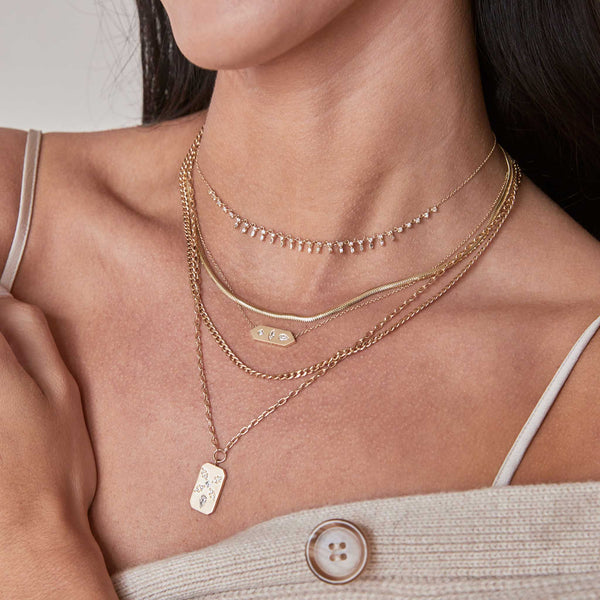woman in a beige sweater wearing a Zoë Chicco 14k Diamond Mosaic Brushed Gold Vertical Dog Tag Square Oval Chain Necklace layered with four other necklaces