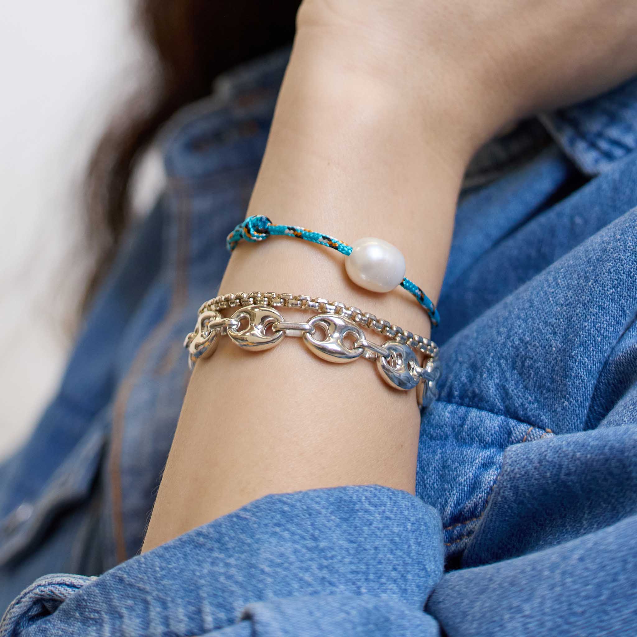 Woman in a denim shirt wearing a Zoë Chicco Sterling Silver Large Puffed Mariner Chain Bracelet stacked with a Sterling Silver Large Box Chain Bracelet and a Medium Baroque Pearl Paracord Bracelet
