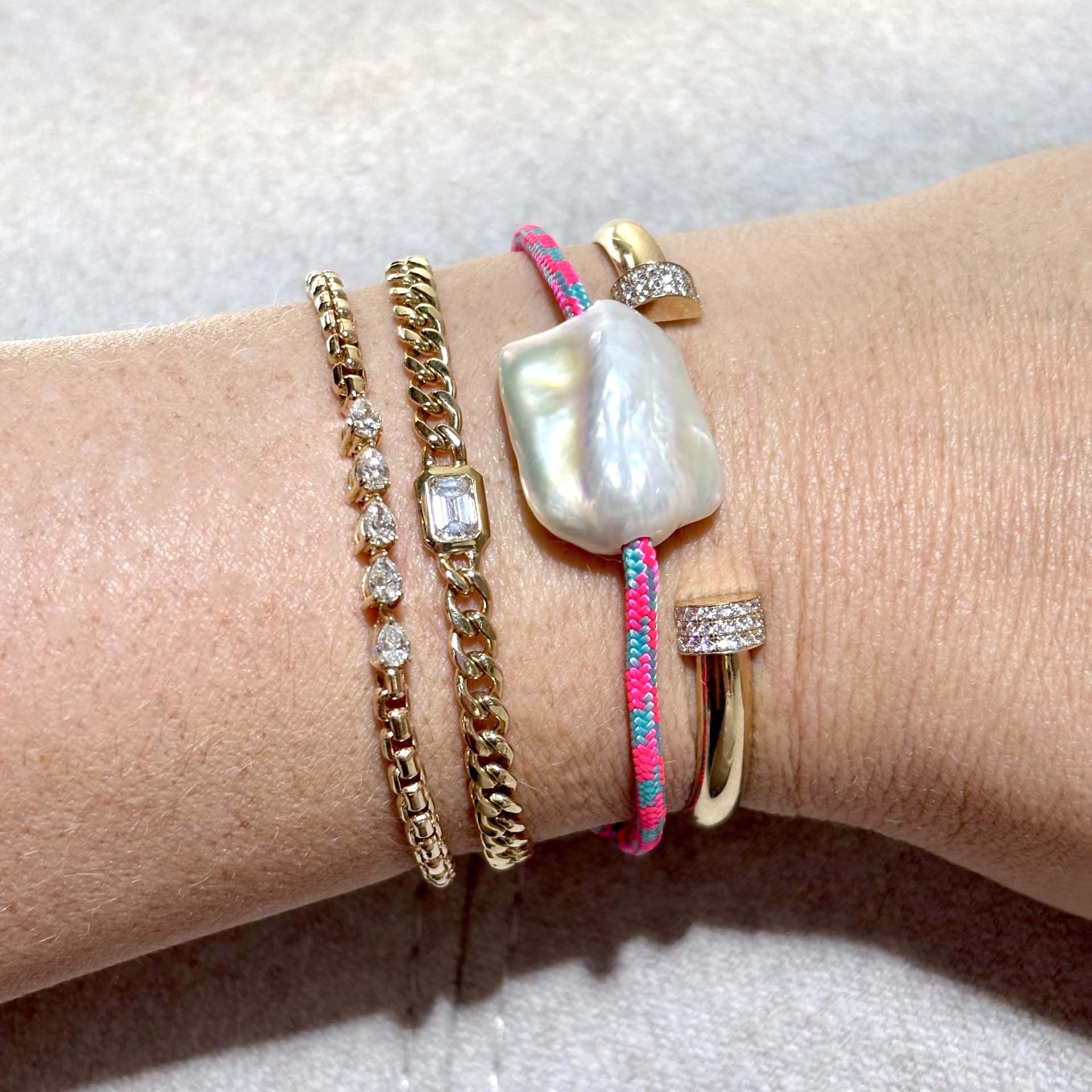 Zoë Chicco Large Flat Baroque Pearl Paracord Bracelet on Pink Blue stacked on a wrist with three other gold and diamond bracelets