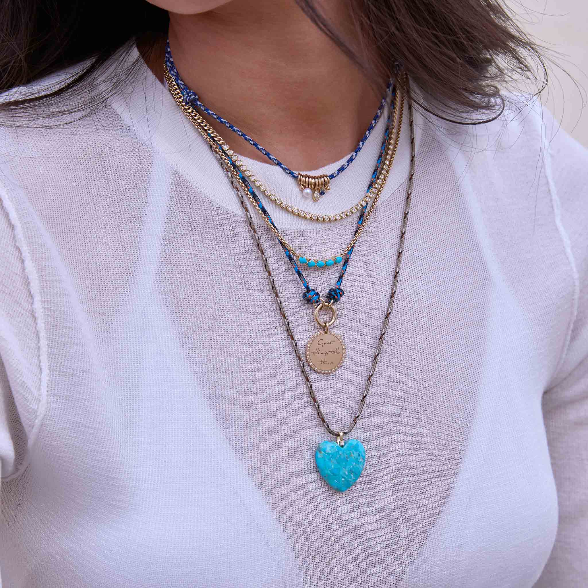Woman wearing Zoe Chicco layered paracord necklaces with beads and a turquoise heart-shaped gemstone with 14k gold and white diamonds against a white shirt