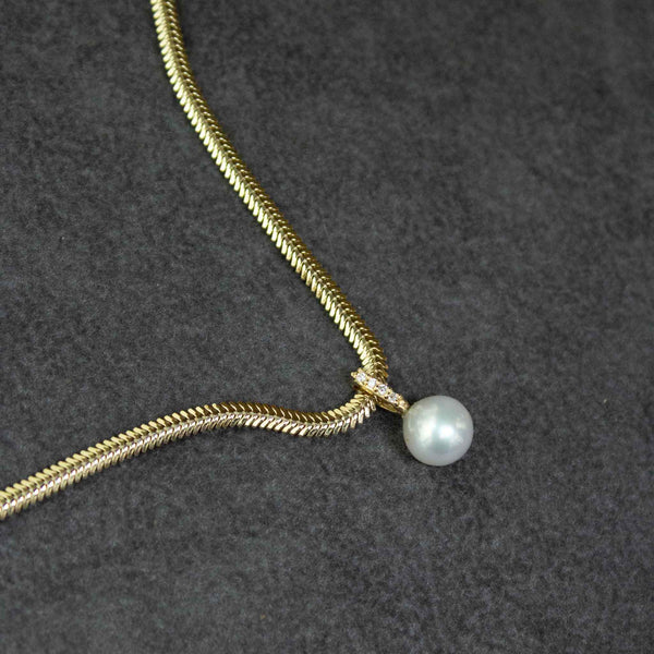 a Zoë Chicco 14k Gold Pearl & Pavé Diamond Bail Snake Chain Necklace laying flat against a dark gray background