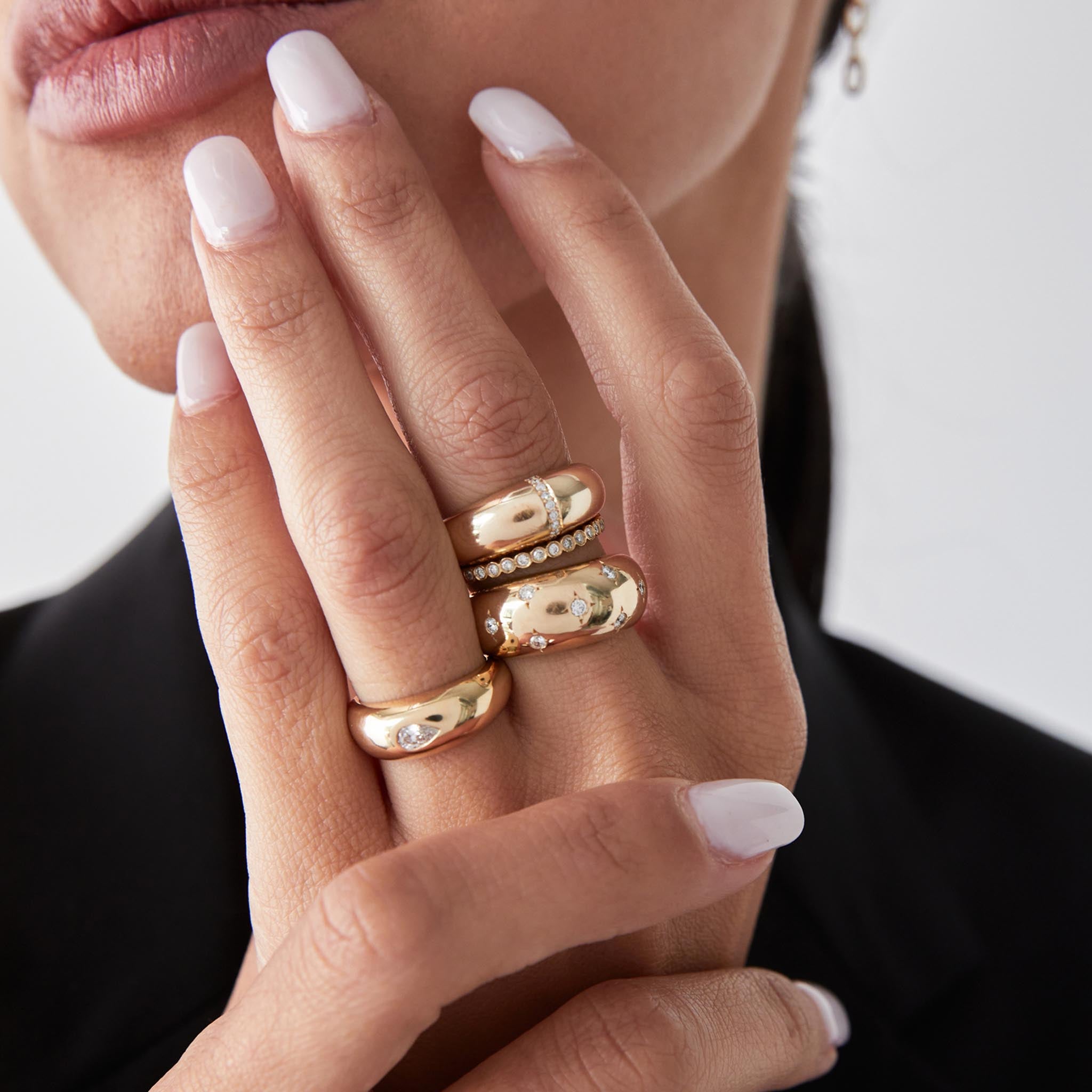 a woman holding her hand up to her chin wearing a Zoë Chicco 14k Yellow Gold Scattered Star Set Diamonds Medium Aura Ring stacked with a Pave Diamond line Small Aura Ring and a Diamond Bezel Eternity Band on her middle finger