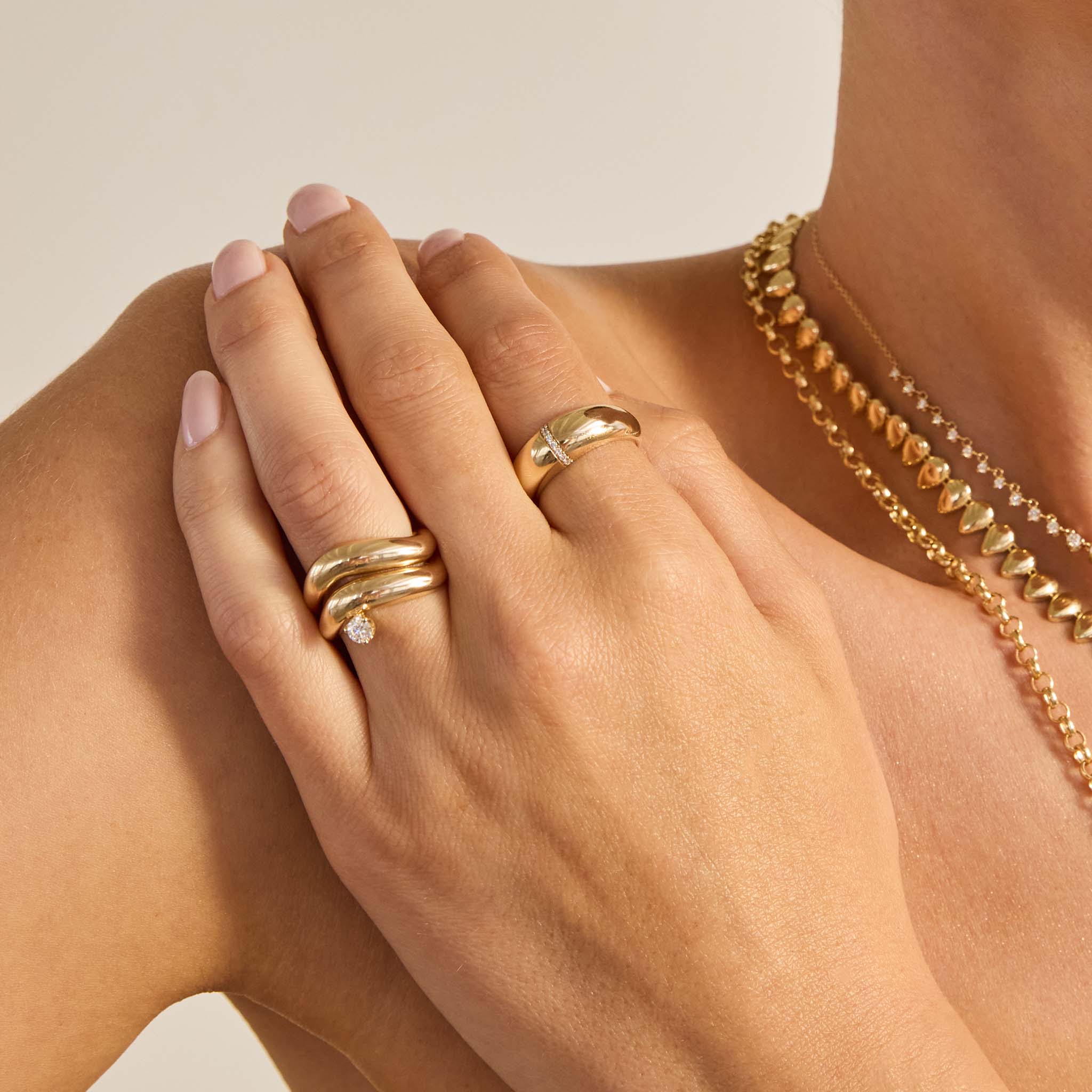 Close up of a woman's hand wearing multiple Zoe Chicco 14k gold stacking rings on a neutral background