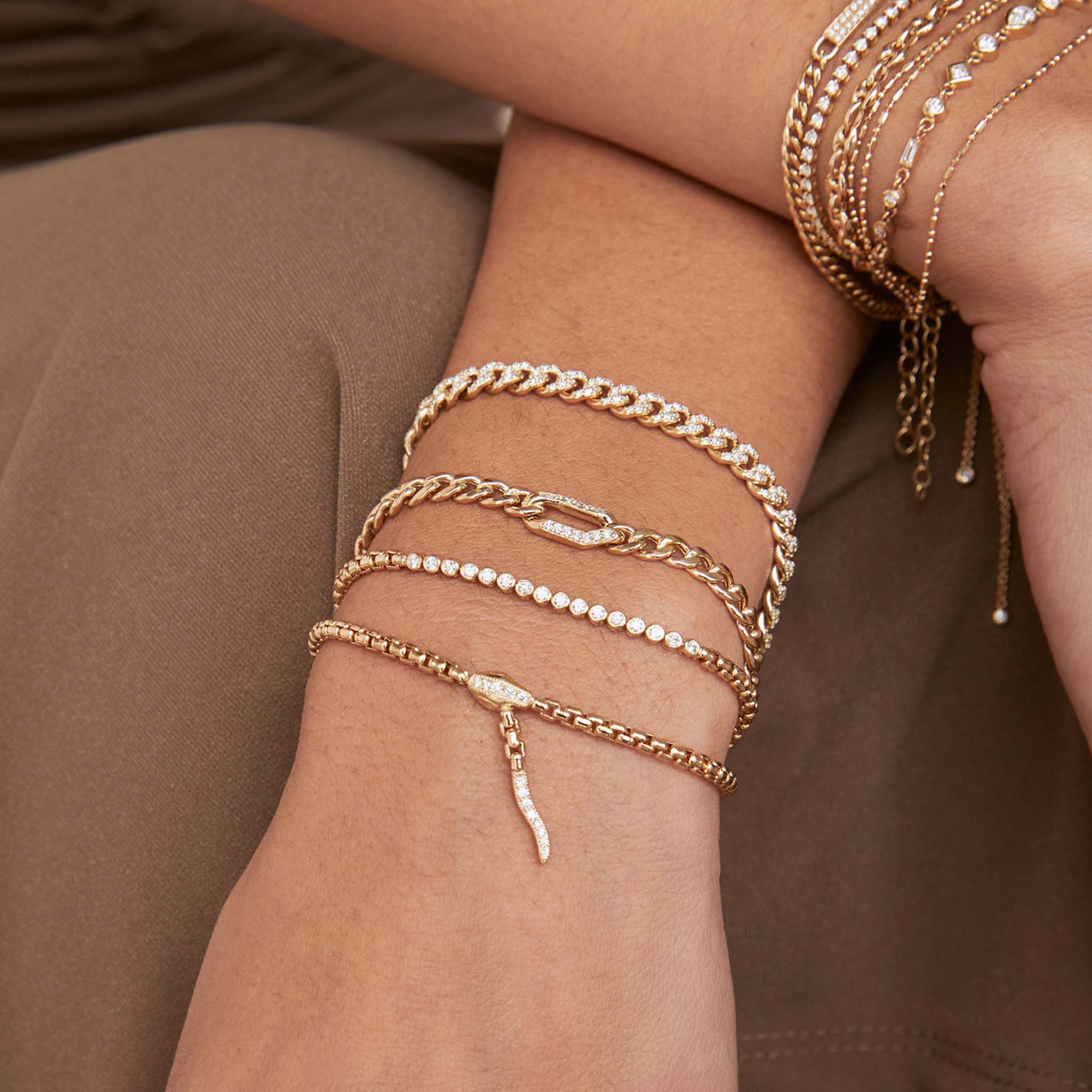 woman's wrist resting on her leg wearing a Zoë Chicco 14k Gold Pavé Diamond Oval Link Medium Curb Chain Bracelet layered with a Snake Box Chain Bracelet, 14k Small Diamond Bezel Tennis Segment Box Chain Bracelet, and a Diamond Bezel Segment Box Chain Bracelet