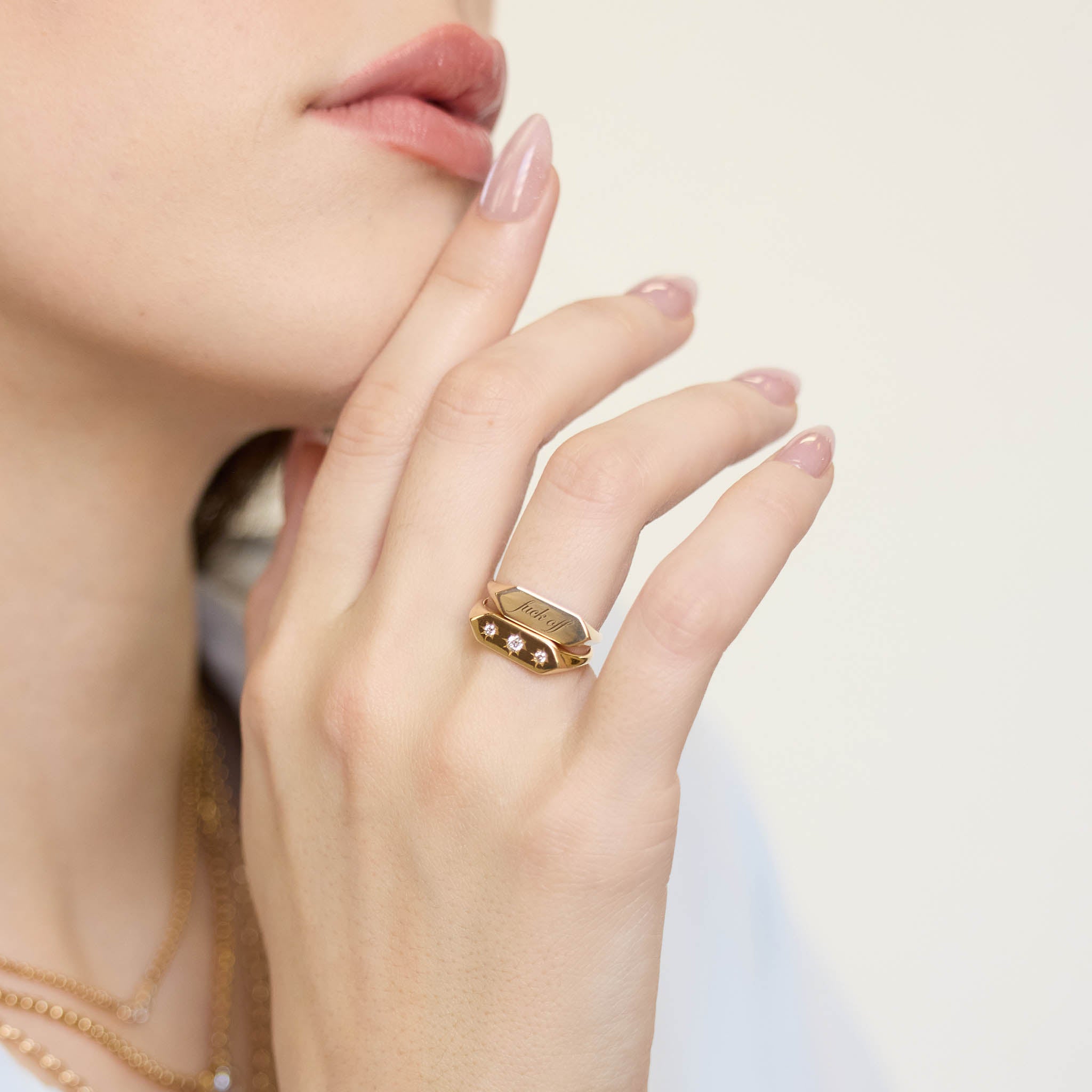 woman's hand resting against her chin wearing a Zoë Chicco 14k Gold "fuck off" Elongated Hexagon Signet Ring stacked with a 14k Graduated Star Set Diamonds Elongated Hexagon Signet Ring on her ring finger