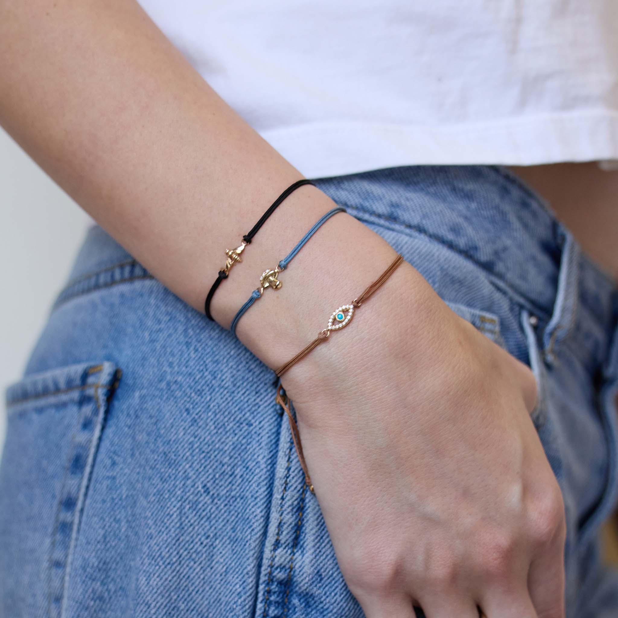 close up of a woman's wrist wearing a Zoë Chicco 14k Gold Bee Thick Cord Bracelet in Black stacked with a 14k Turquoise & Diamond Evil Eye Cord Bracelet in Taupe and a 14k Diamond Mushroom Thick Cord Bracelet in Ocean Blue
