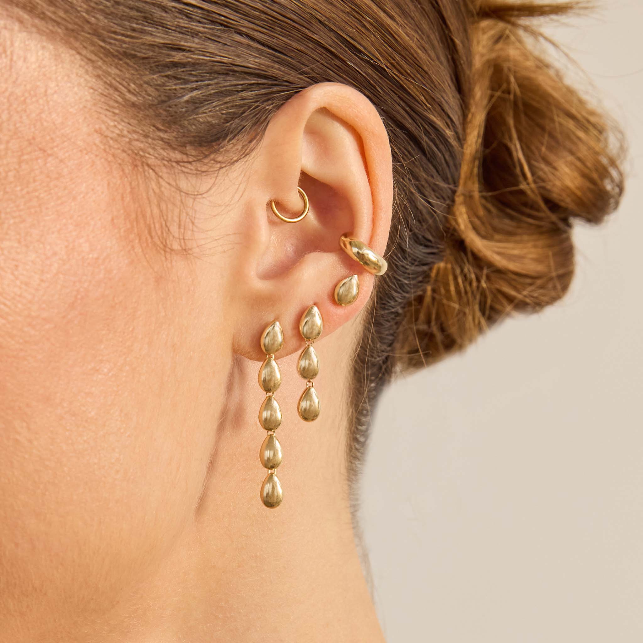 Close-up of a person wearing Zoe Chicco 14k gold hoop earrings and teardrop shaped dangling earrings with a neutral background