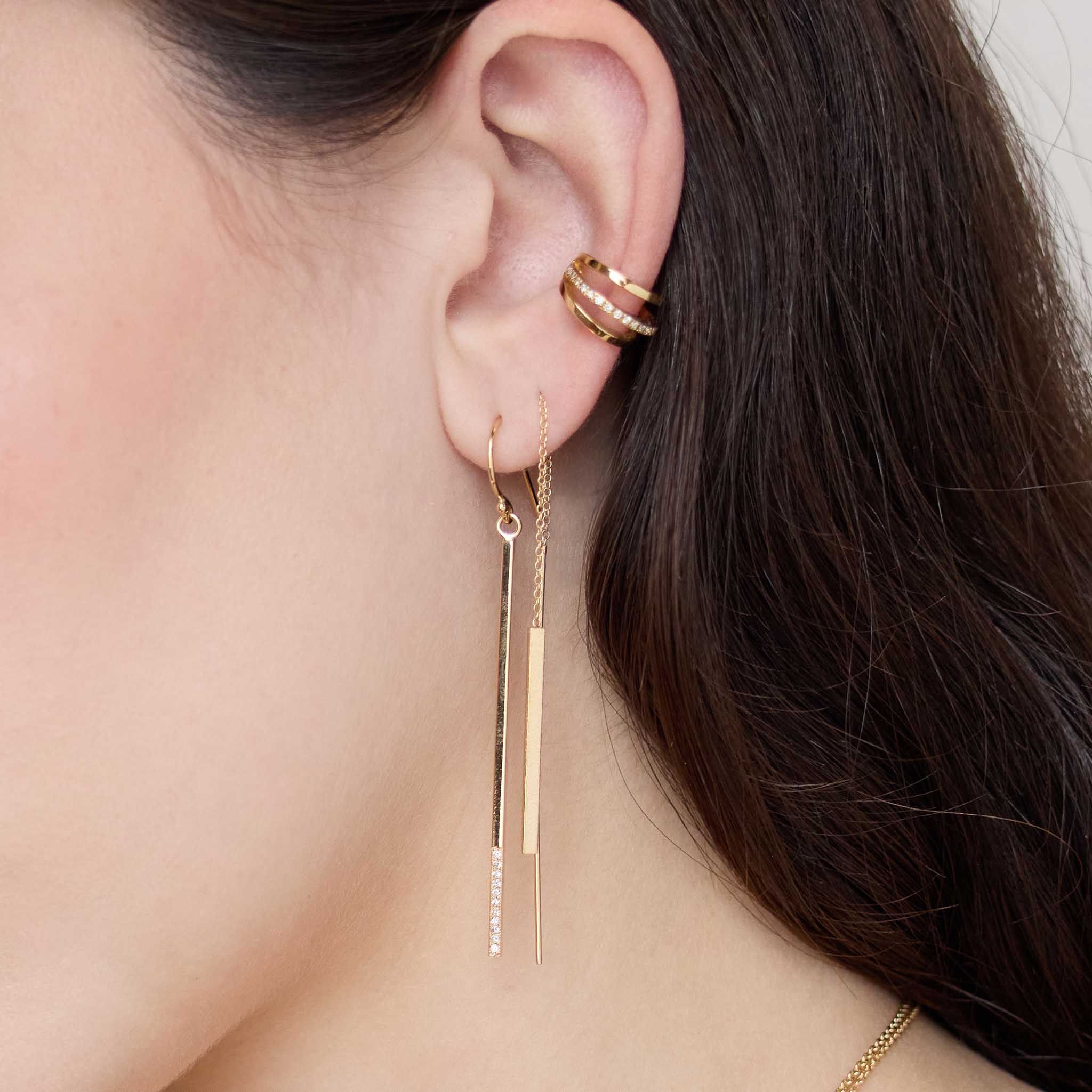 Close up of a woman's ear wearing Zoe Chicco 14k gold bar dangle earrings with pave diamonds