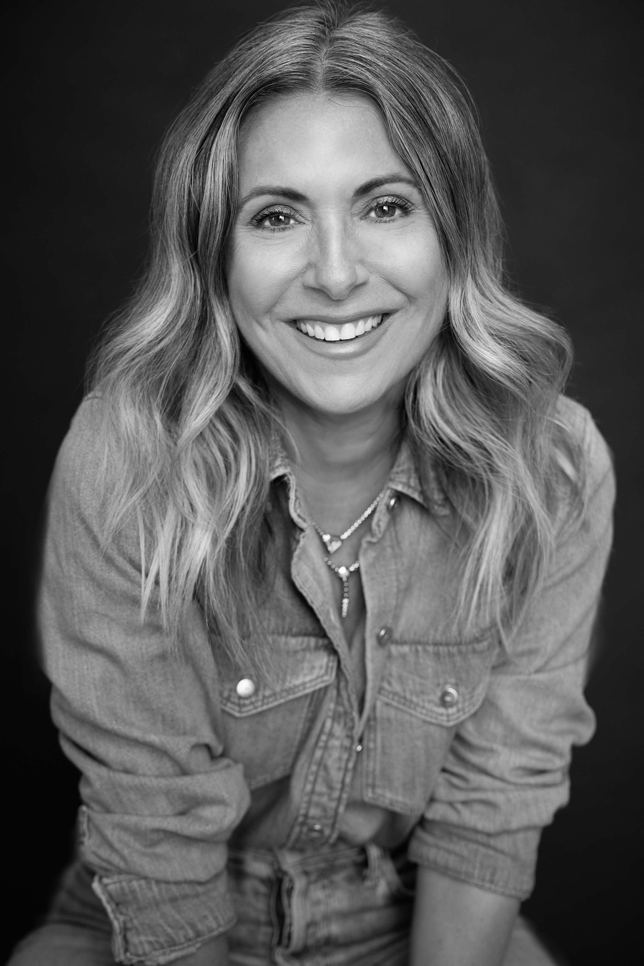 Black and white portrait of a woman with wavy hair wearing a denim jacket.