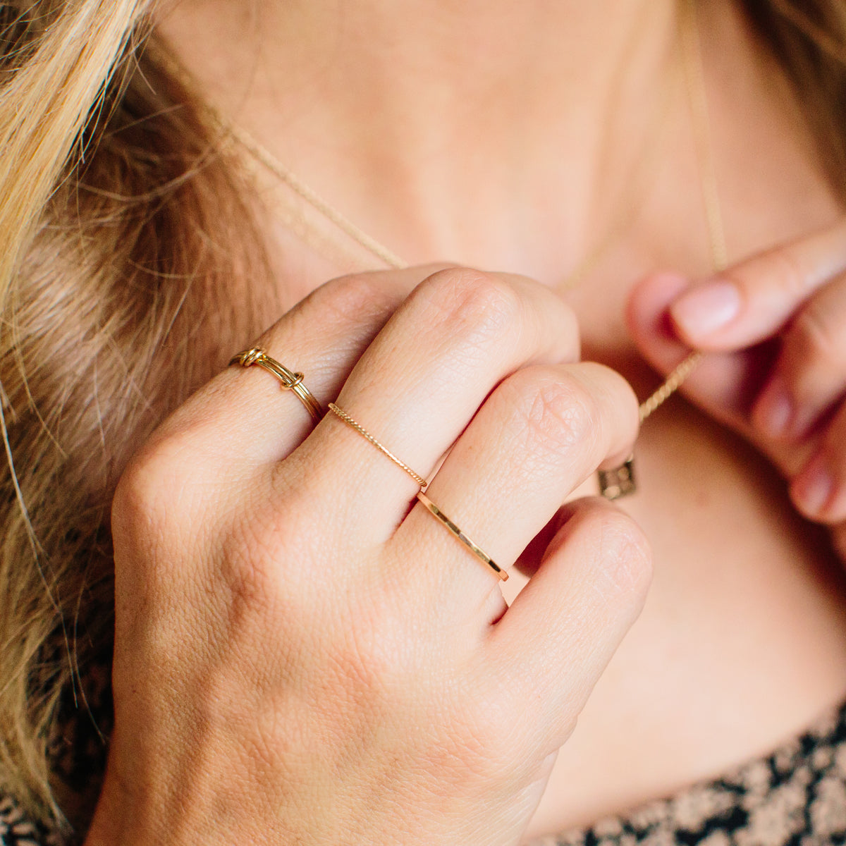 close up of woman's hand wearing Zoë Chicco 14k Gold Thin Hammered Band Ring with two other gold rings