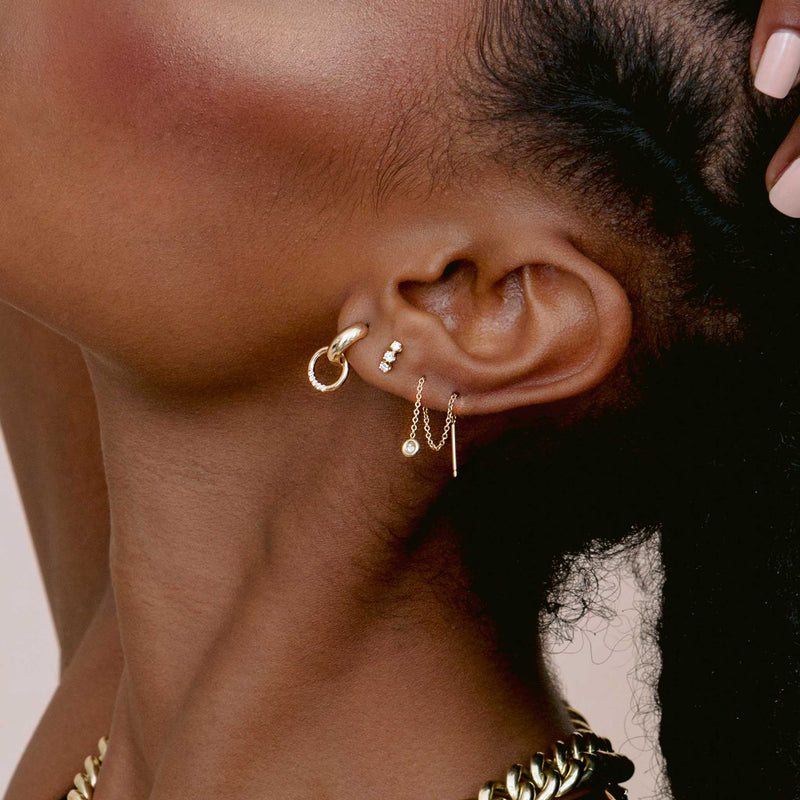 woman wearing a Zoë Chicco 14k Gold Floating Diamond Threader Earring looped through two piercings and layered with two other earrings