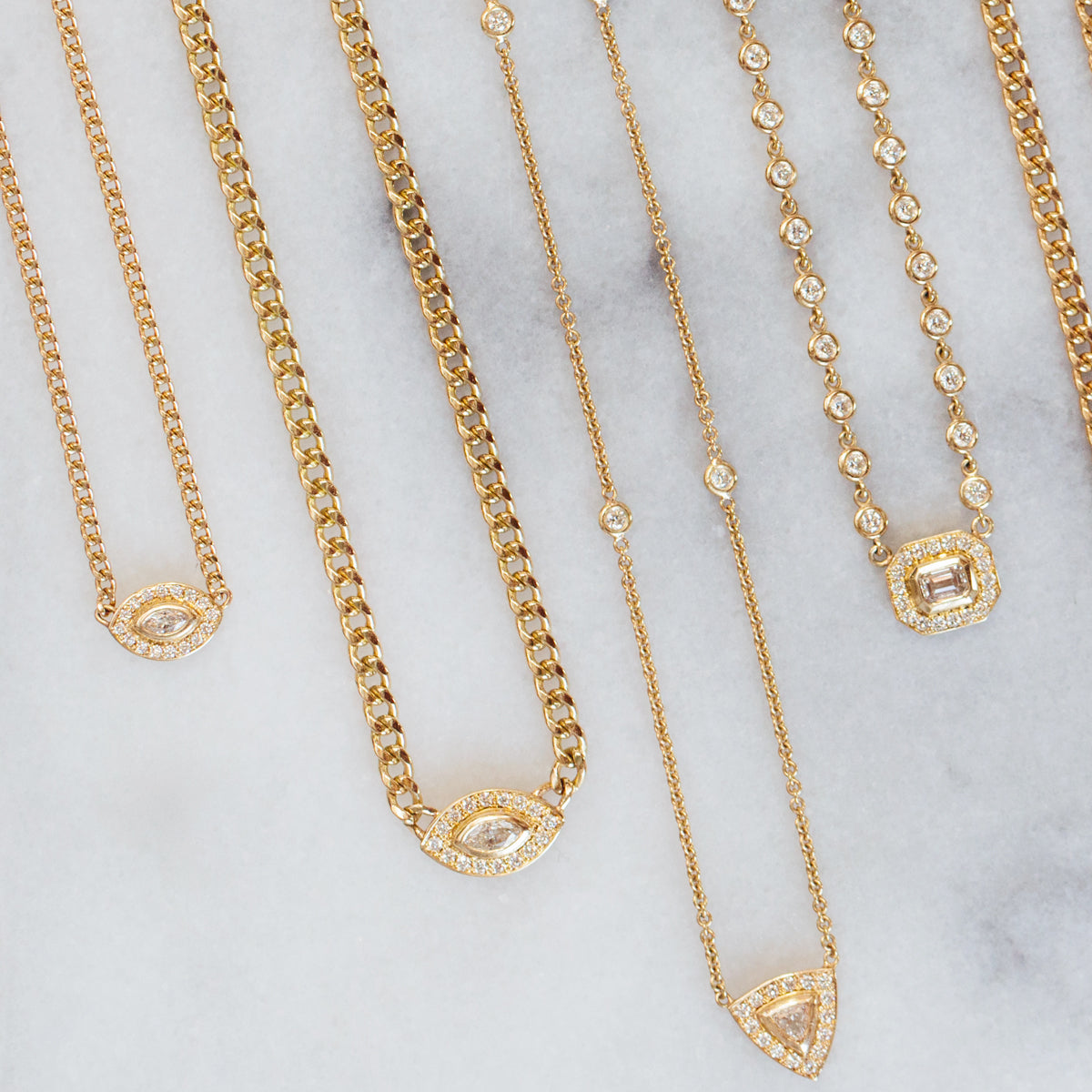 a flat lay image of Zoë Chicco 14k Gold Marquise Diamond Halo Curb Chain Necklace against a marble background