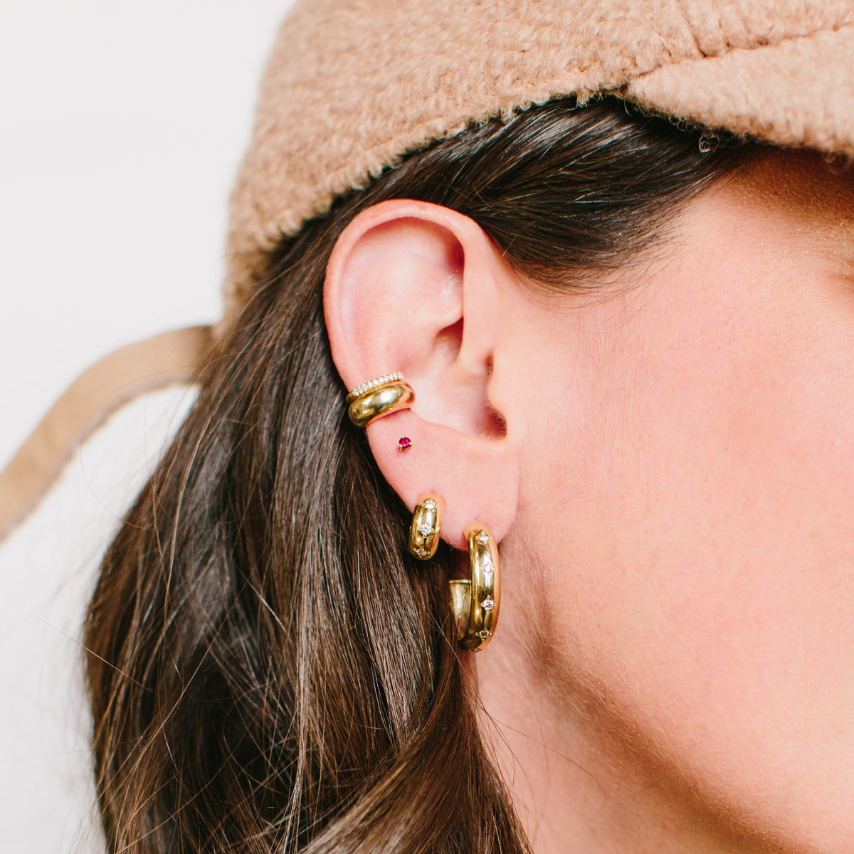 Woman's ear wearing Zoe Chicco 14kt Gold Ruby Prong Stud with chubby wide huggie hoops