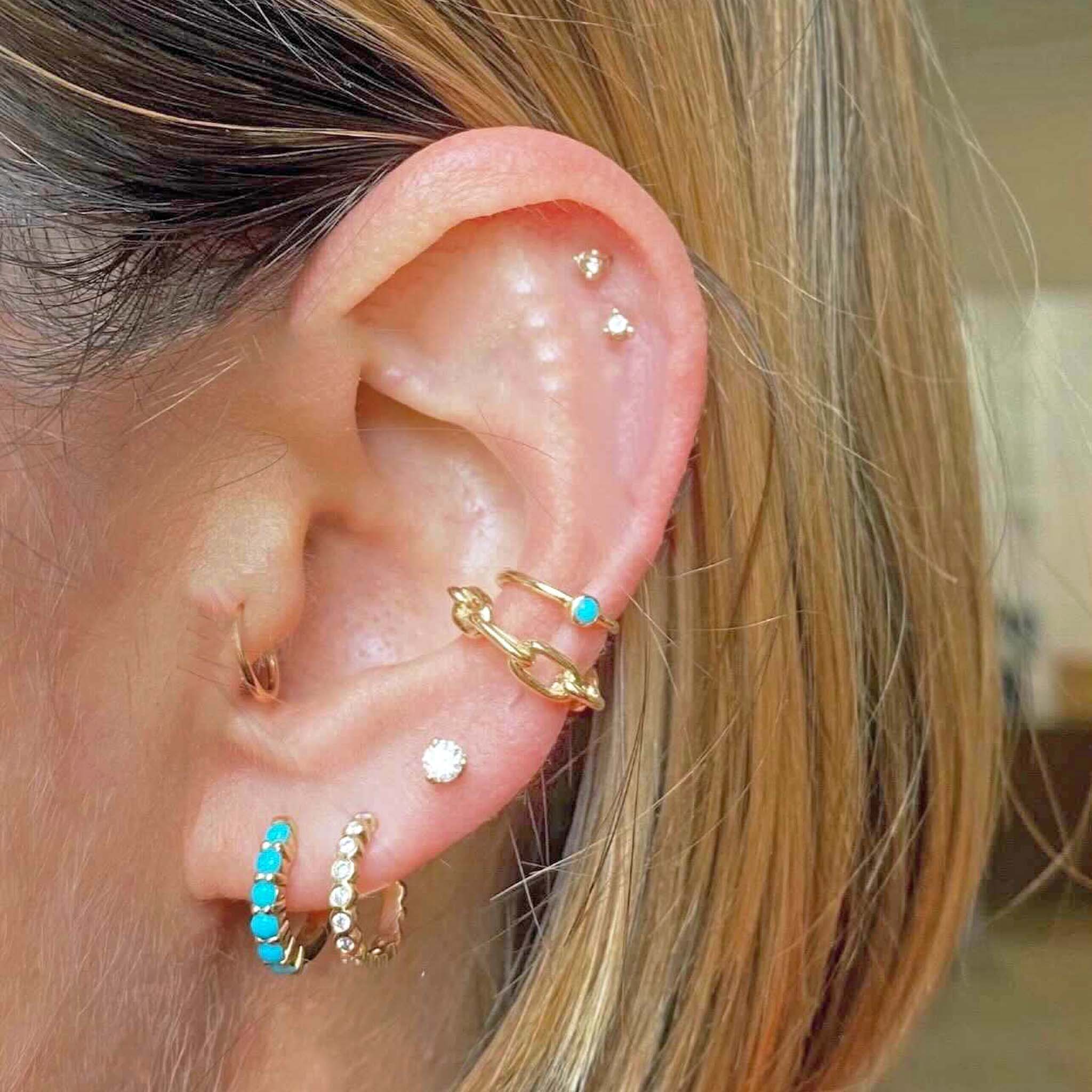 woman's ear wearing Zoë Chicco 14k Gold Turquoise Bezel Ear Cuff layered with a square oval link cuff and diamond and turquoise earrings