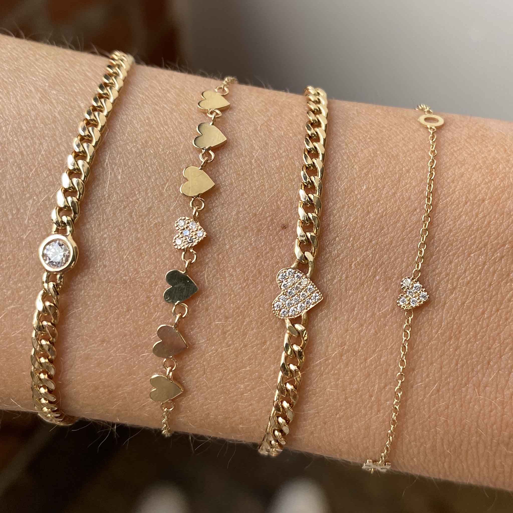 woman's wrist wearing a Zoë Chicco 14k Gold 7 Itty Bitty Gold & Pavé Diamond Linked Hearts Bracelet layered with a 14k Midi Bitty Pavé Diamond Heart Small Curb Chain Bracelet and 14k Itty Bitty XO & Pavé Diamond Heart Bracelet